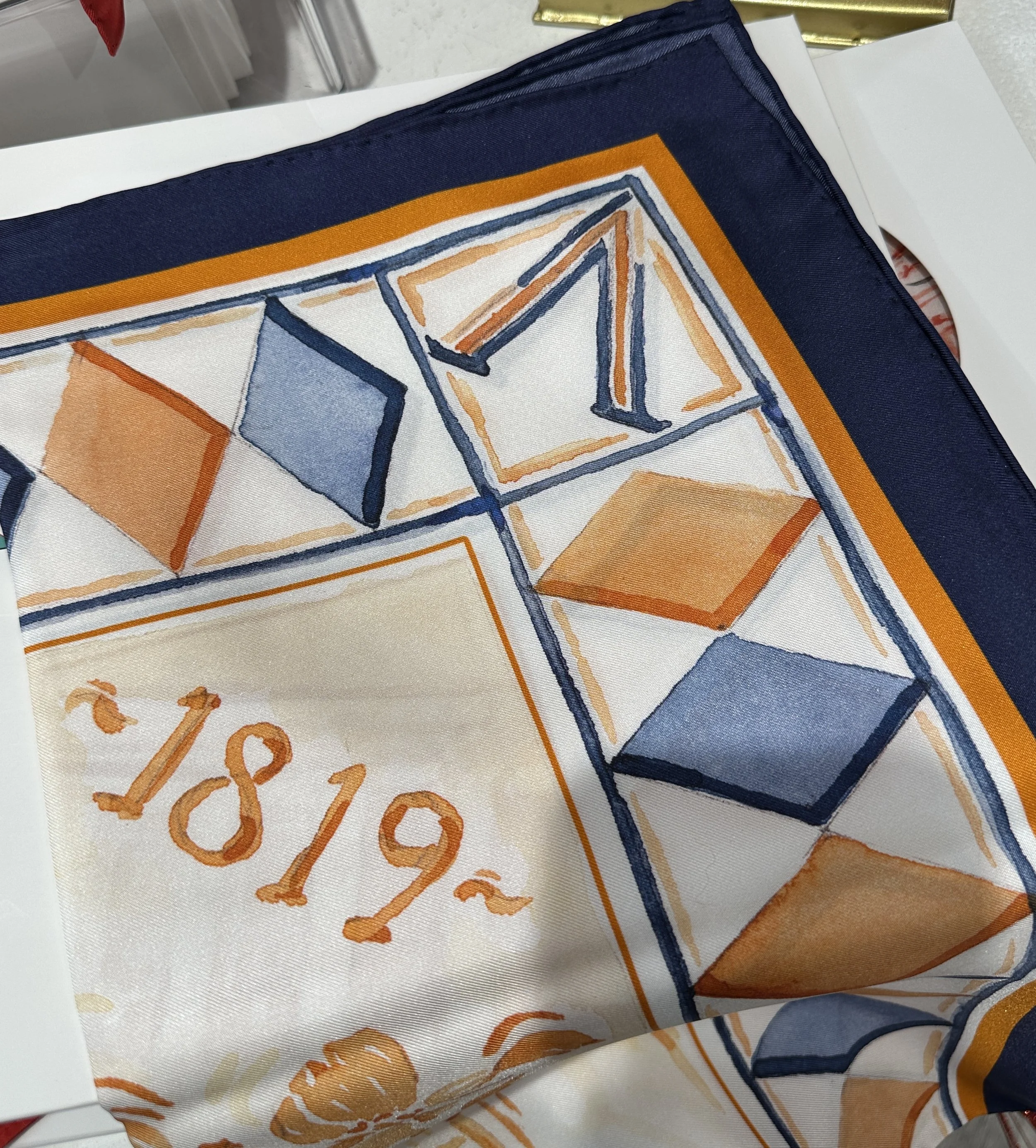 UVA watercolor silk scarf by Megan Grinder, shown on the diamond, with the Rotunda and dogwood blossoms in orange inside a navy diamond border