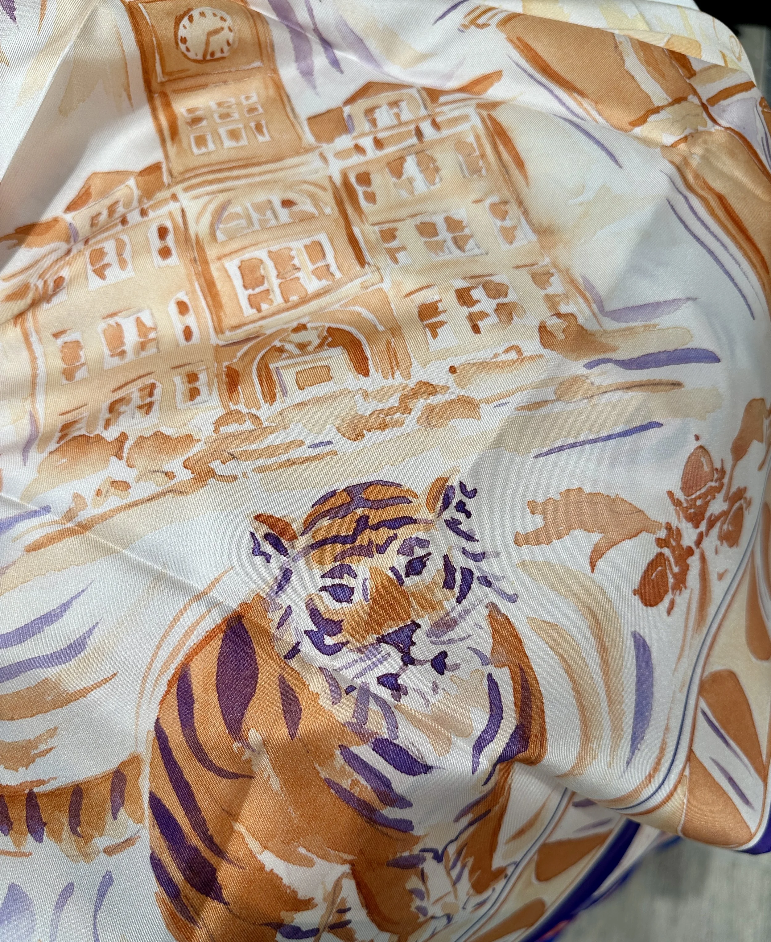 Clemson watercolor silk scarf by Megan Grinder, shown on the diamond, with tigers and Tillman Hall in orange and purple inside a purple border