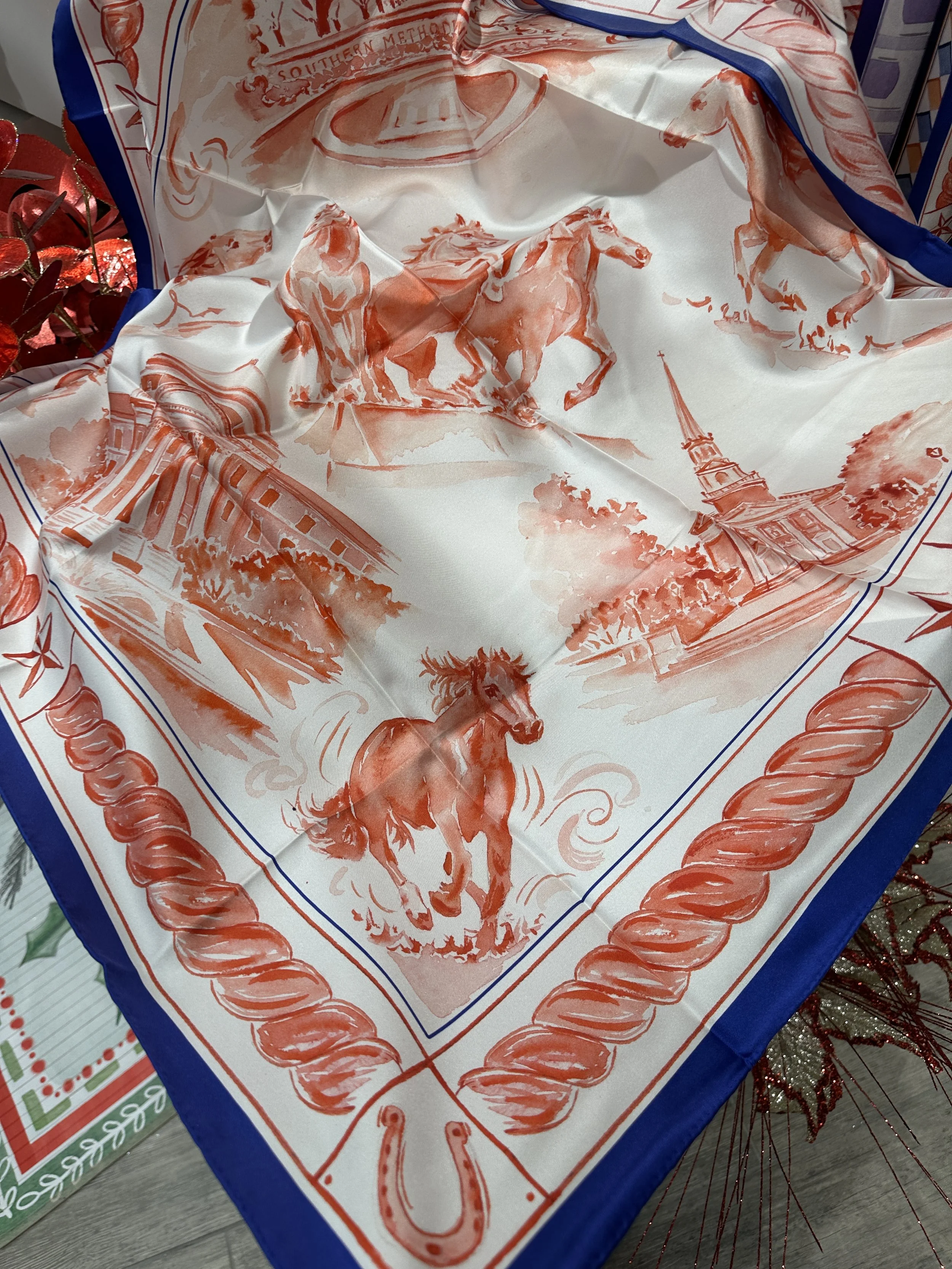 SMU watercolor silk scarf by Megan Grinder, shown on the diamond, with galloping mustangs and Dallas Hall in red inside a navy border