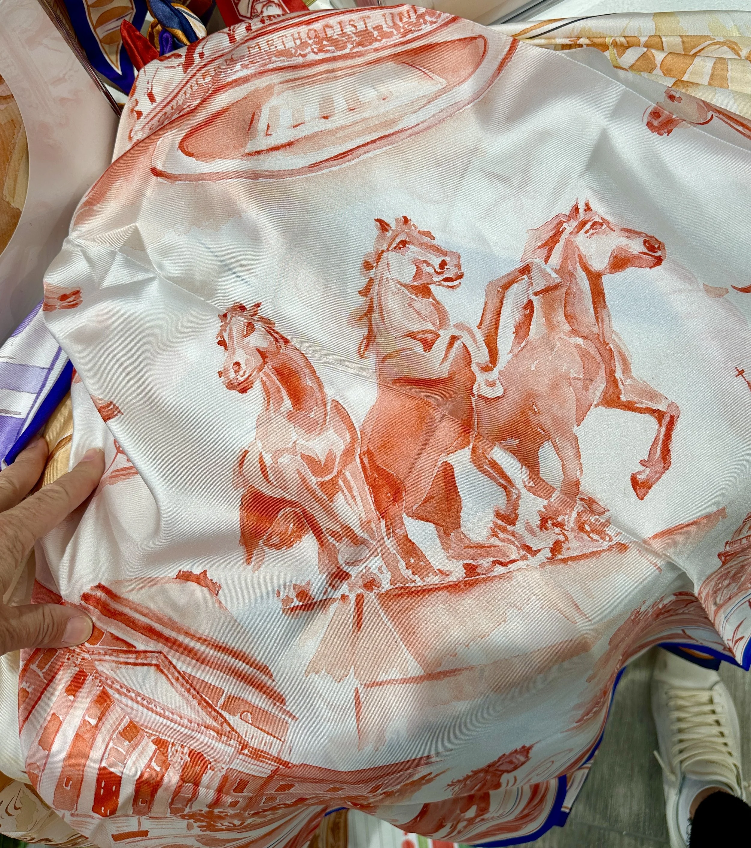SMU watercolor silk scarf by Megan Grinder, shown on the diamond, with galloping mustangs and Dallas Hall in red inside a navy border
