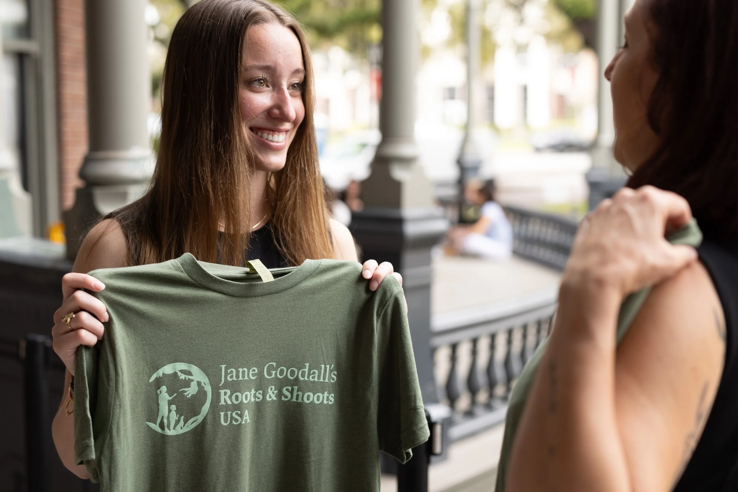young woman holding shirt that reads "jane goodall roots & shoots USA"