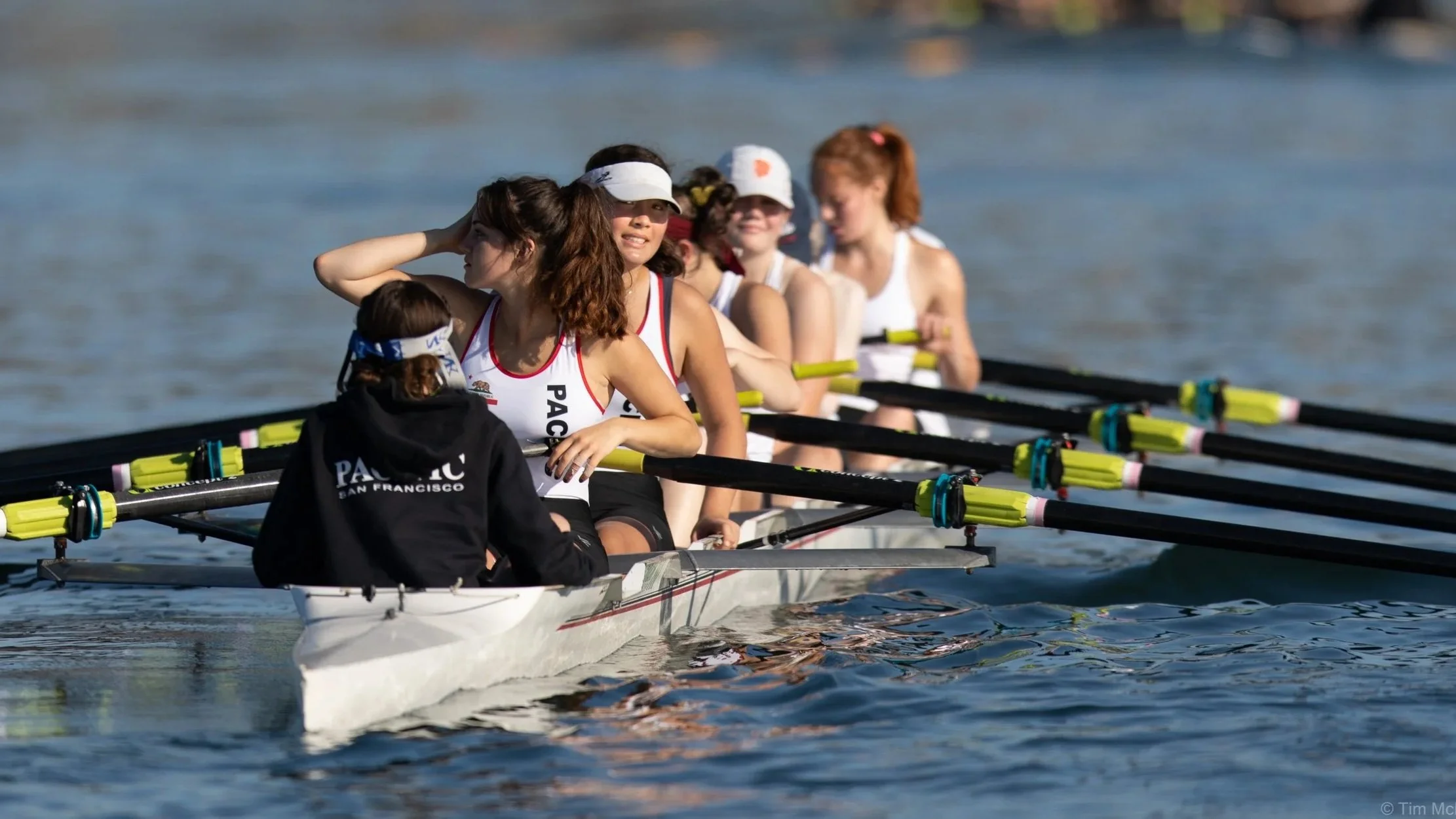 girls sitting in a boat wearing pacific uniform, smiling at the camera