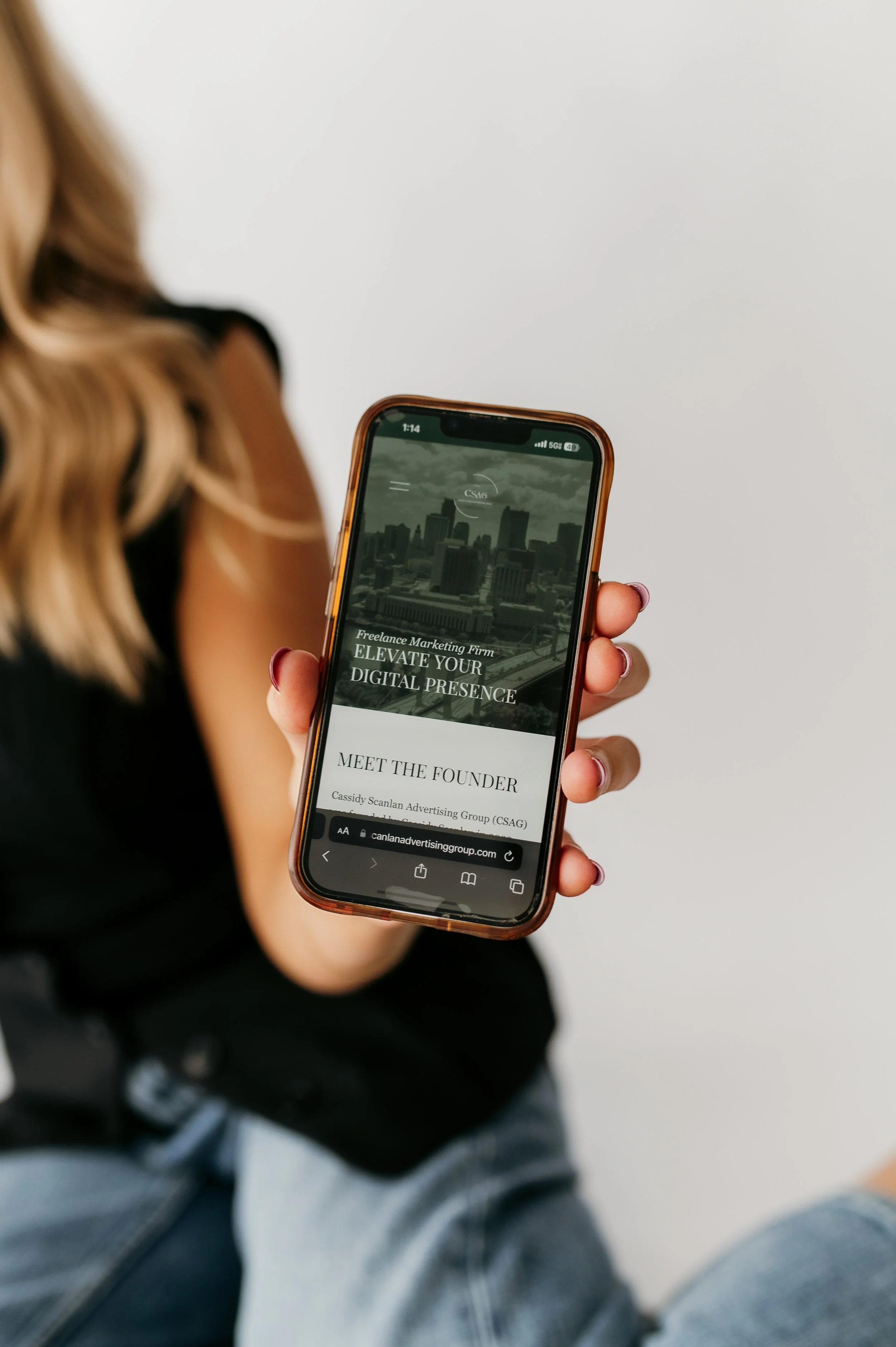 A woman holding a smartphone displaying a website for a freelance marketing firm, with a city skyline on the screen.