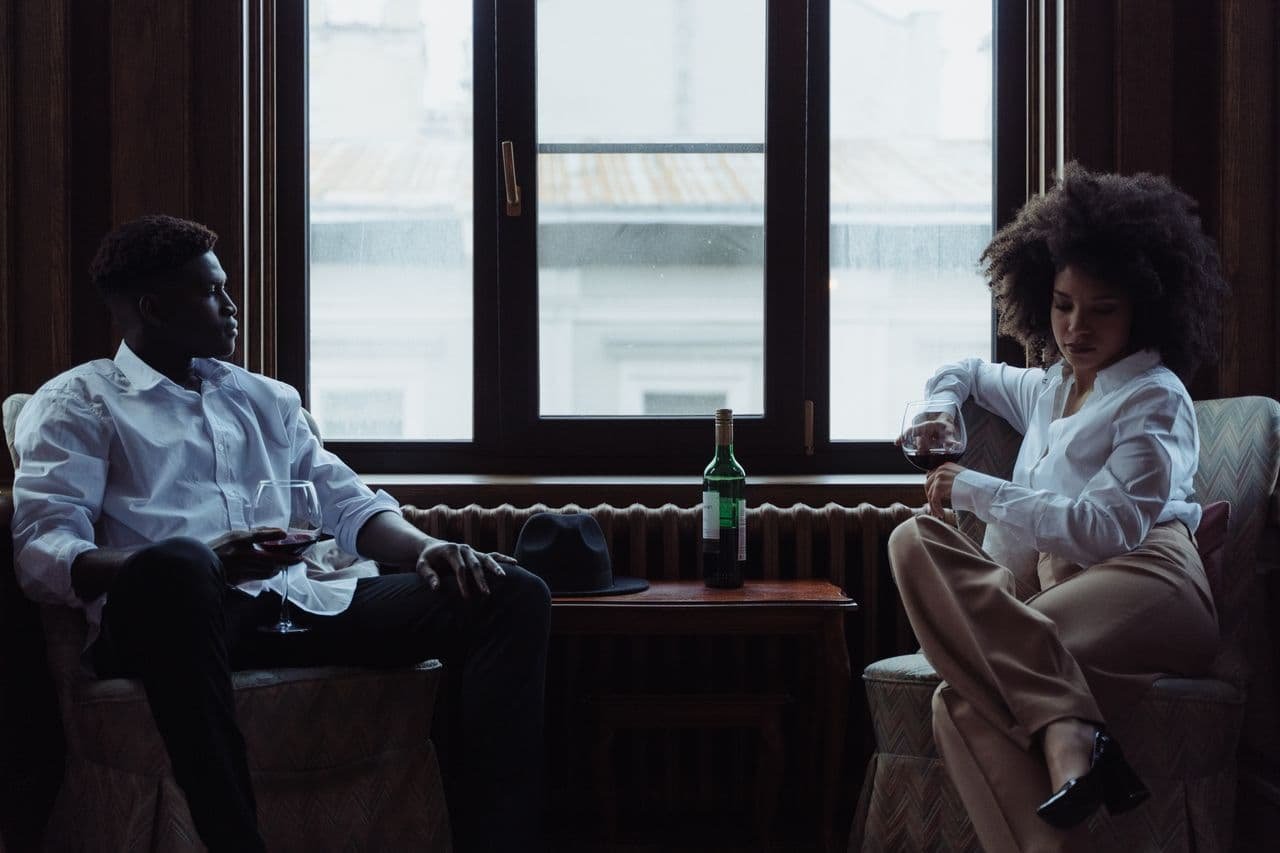 man-and-woman-in-white-dress-shirts-sitting-on-sofa-chairs-holding-glasses-of-wine