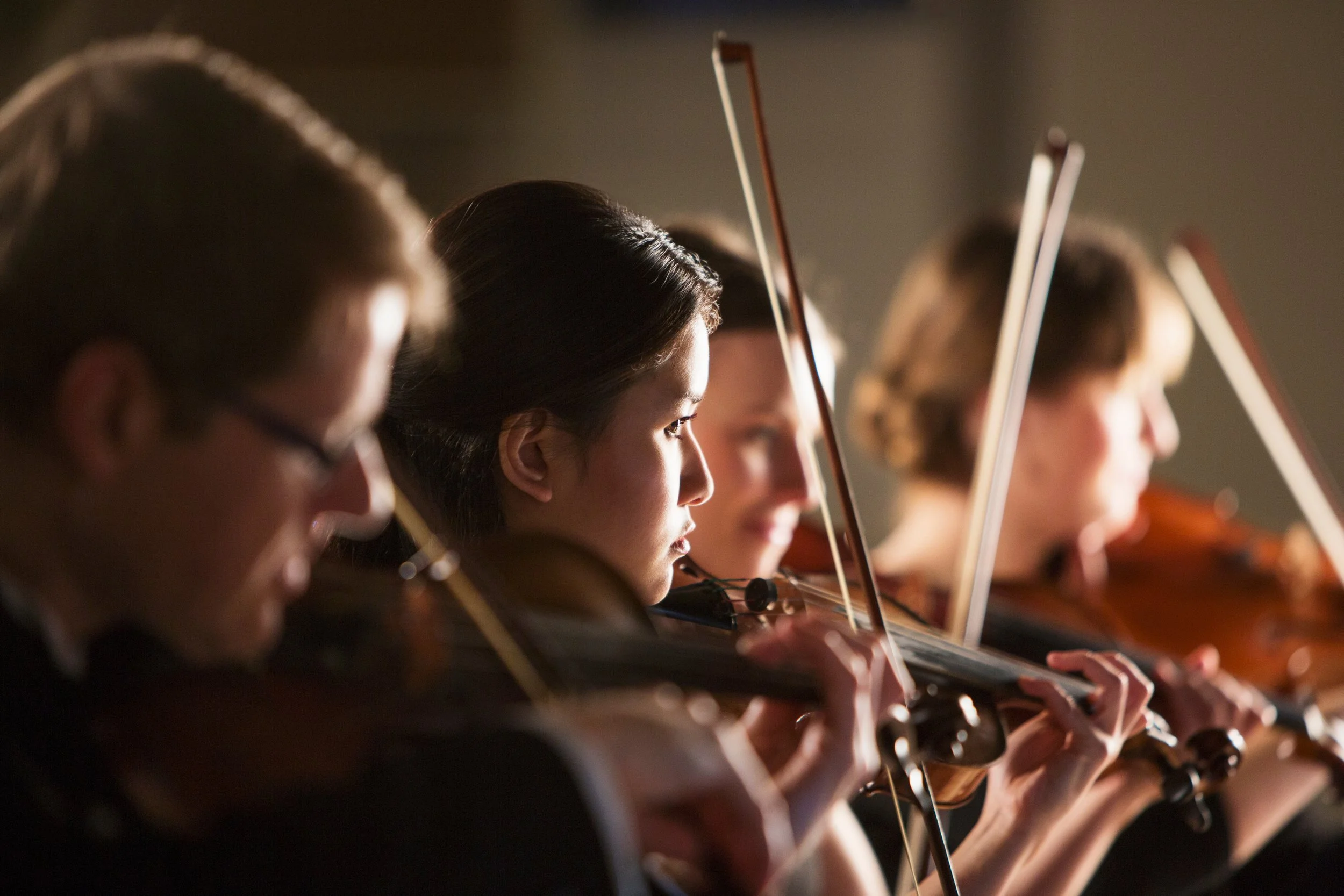 College orchestra students rehearsing violin section during ensemble practice.