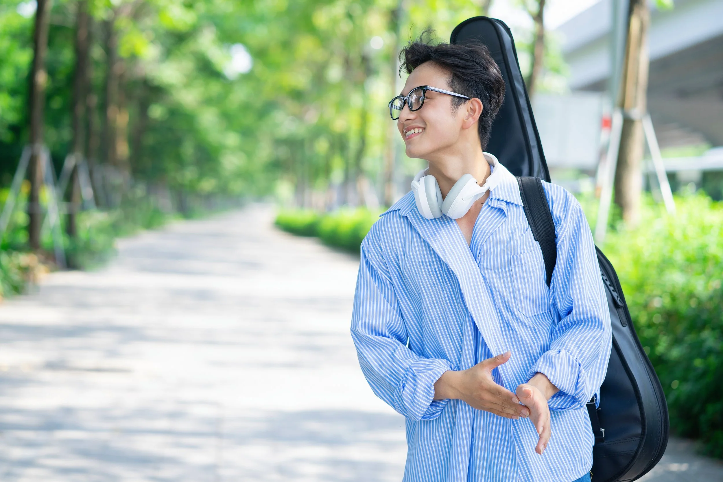 Student musician walking outdoors with instrument case and headphones, preparing for college music opportunities.