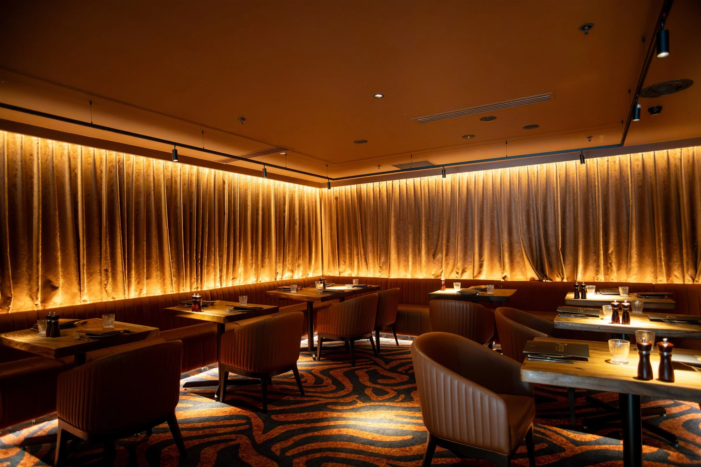 Main dining room at 7 Cutz Steakhouse Canberra with leather banquette seating, timber tables and warmly lit velvet curtains for group dining