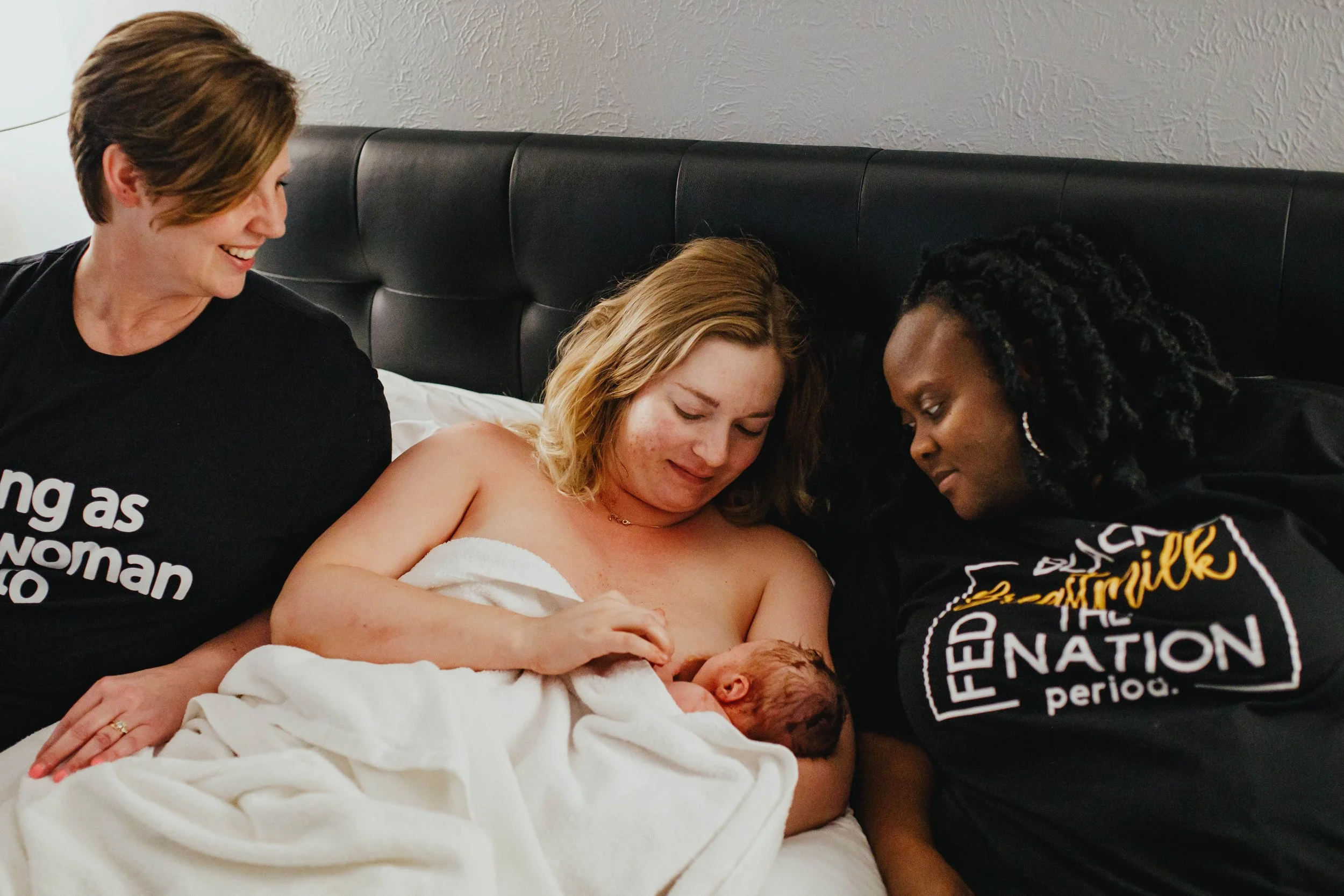 mother holds baby and breastfeeds while midwife helps