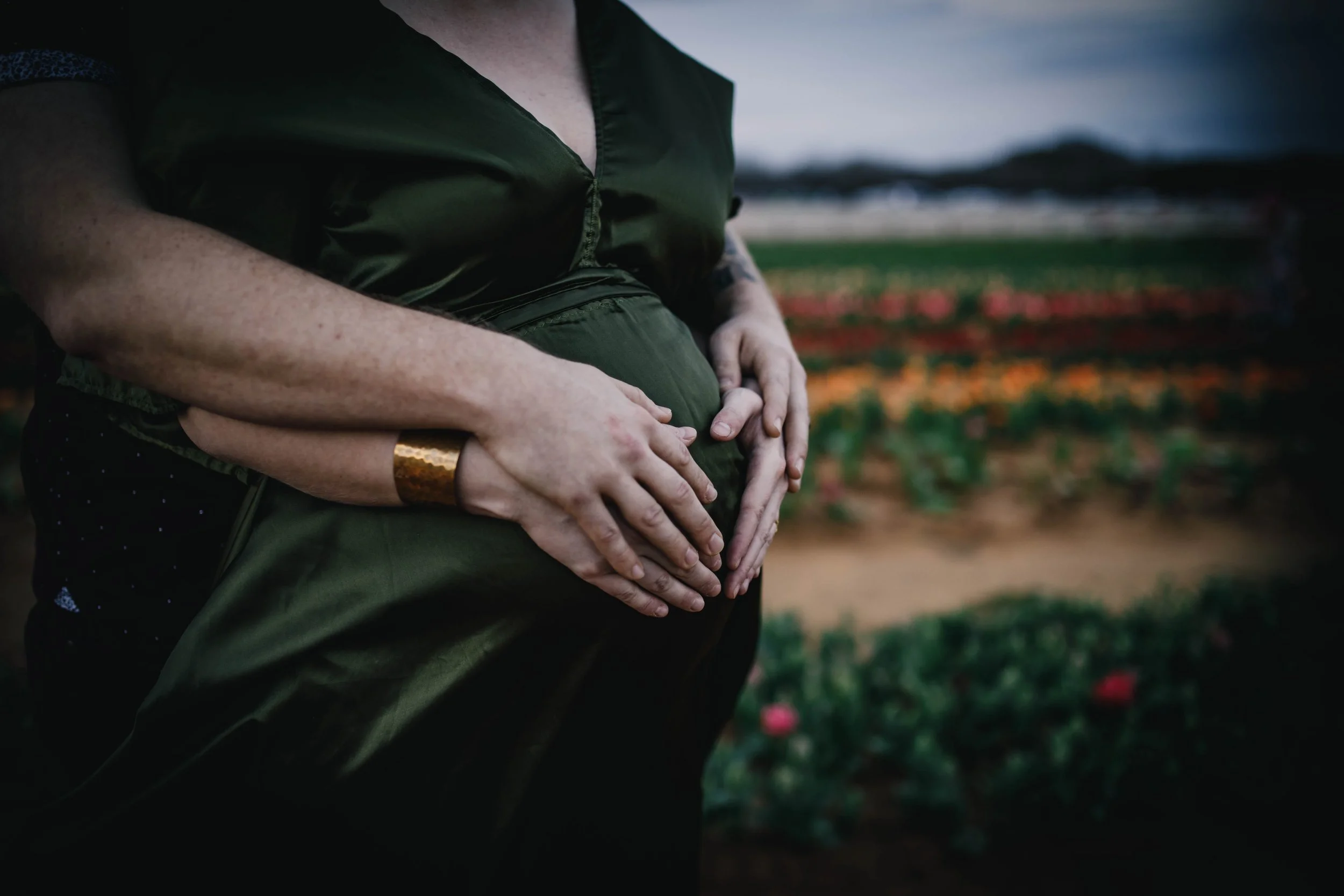 pregnant mom and father holding belly in field maternity pictures