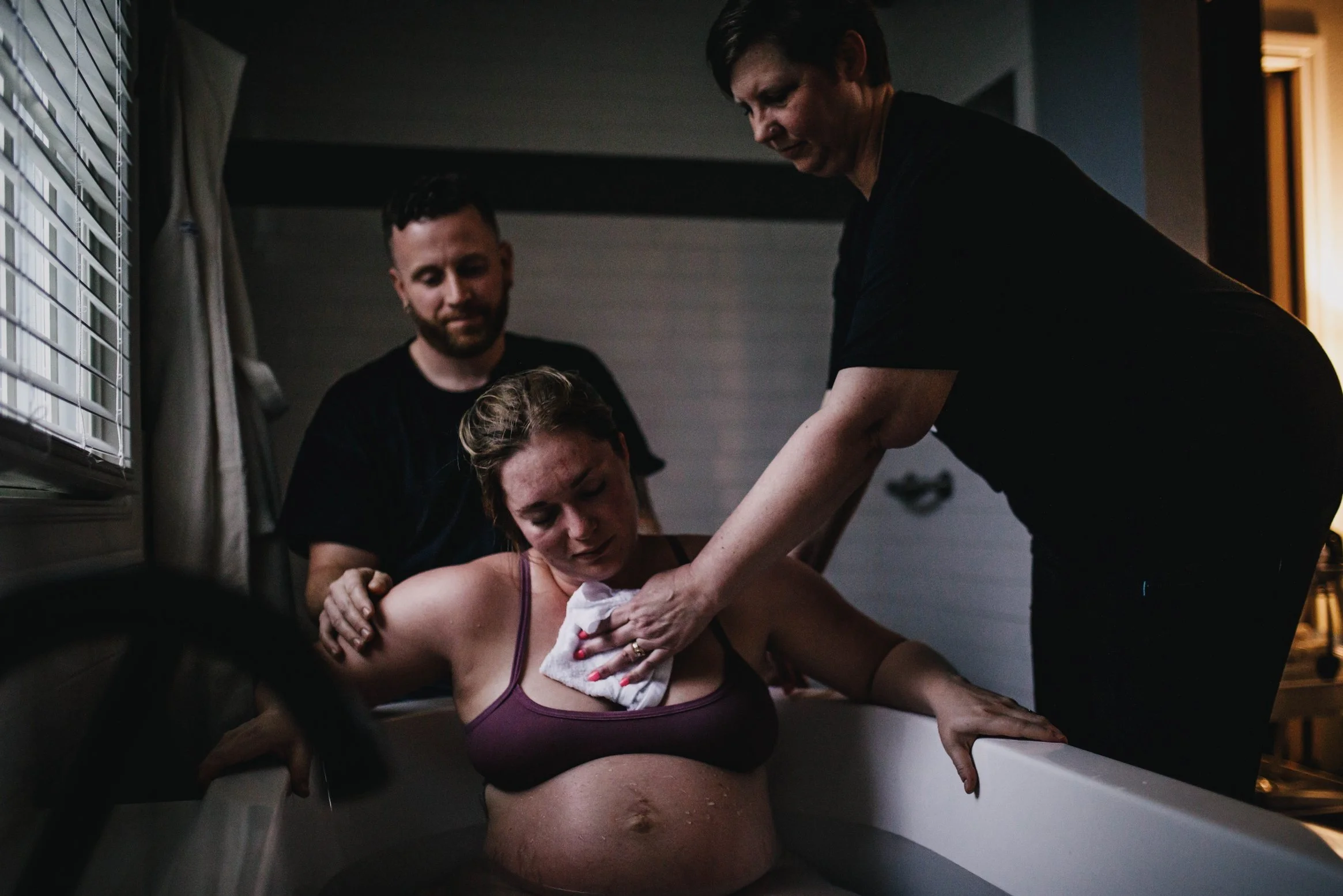 mother labors in birth tub while supported by husband and doula