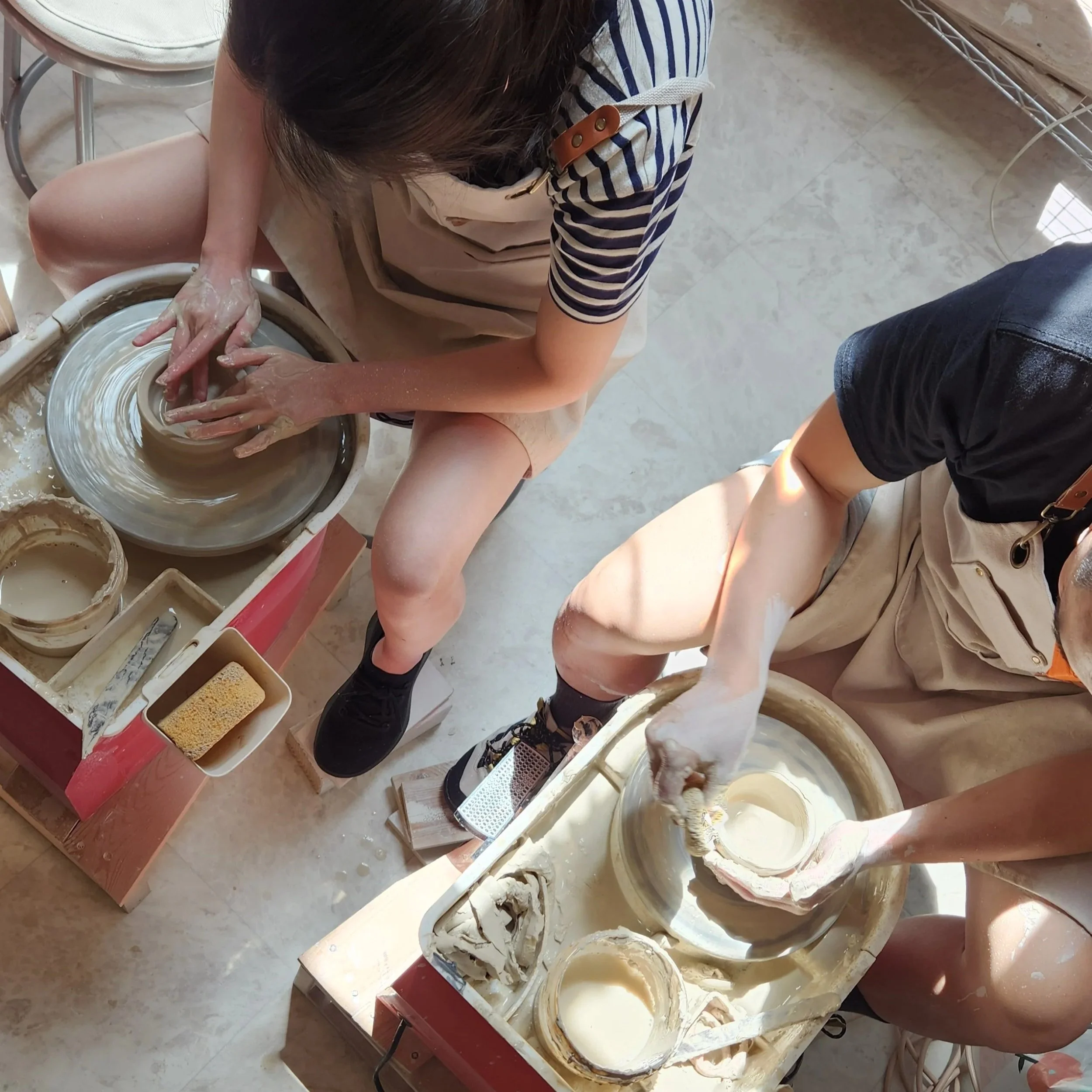 Two friends throwing on the potter’s wheel trying ceramics pottery fun date Oakland pottery class