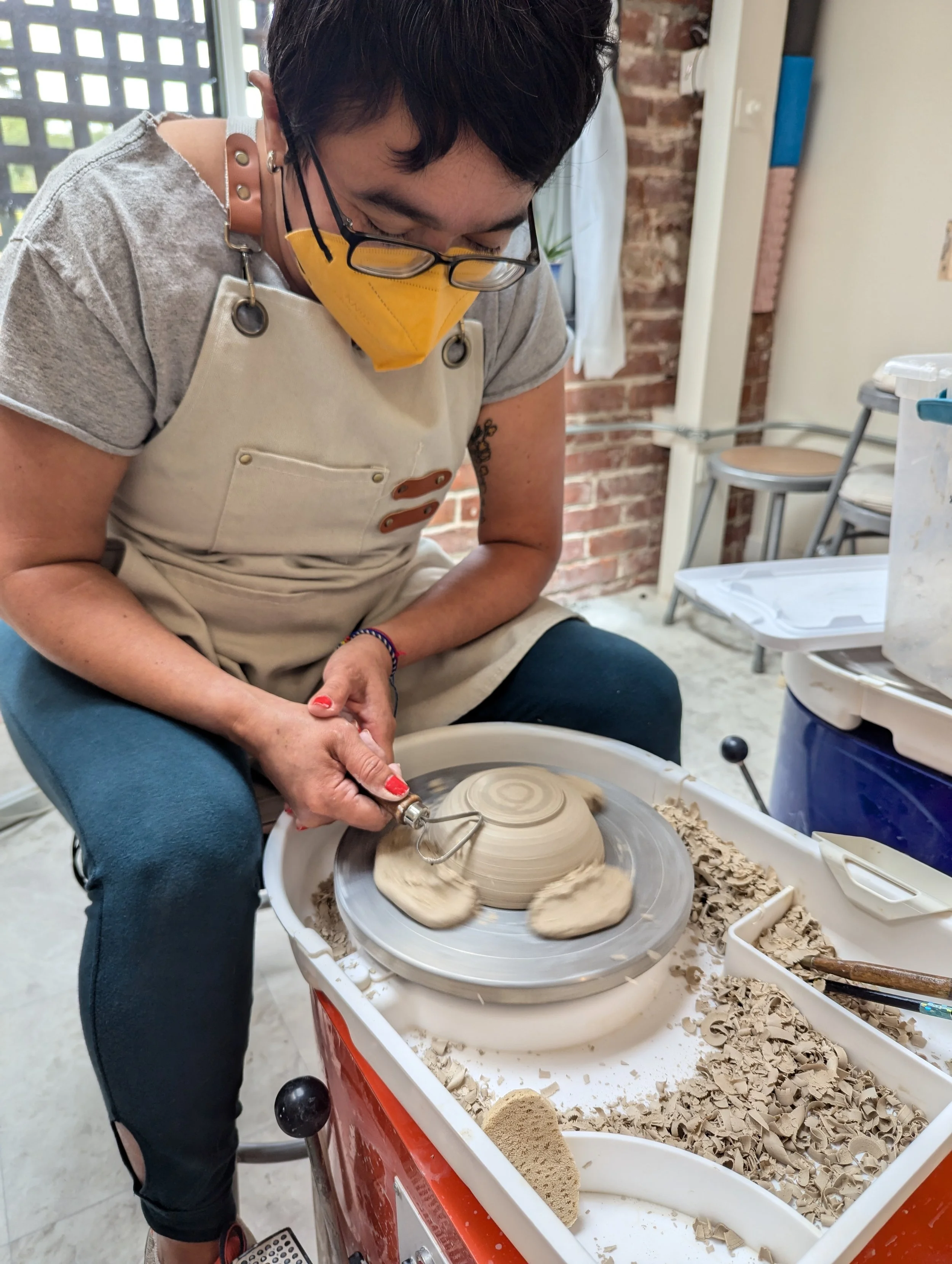 A regular student at Waveform trims their work and plays on the potter’s wheel, creating a bowl
