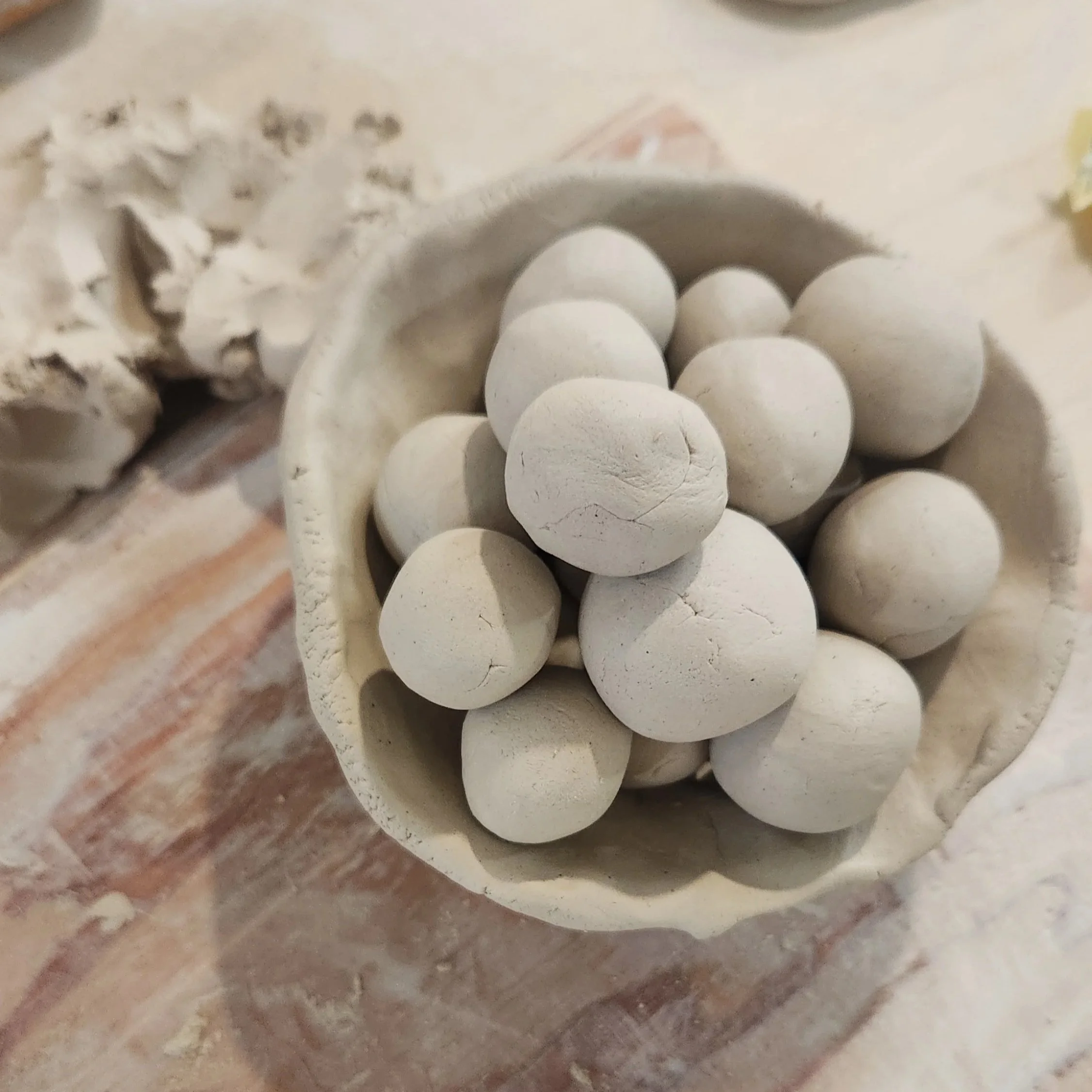 Small balls of clay rest in an unglazed, handmade ceramic bowl