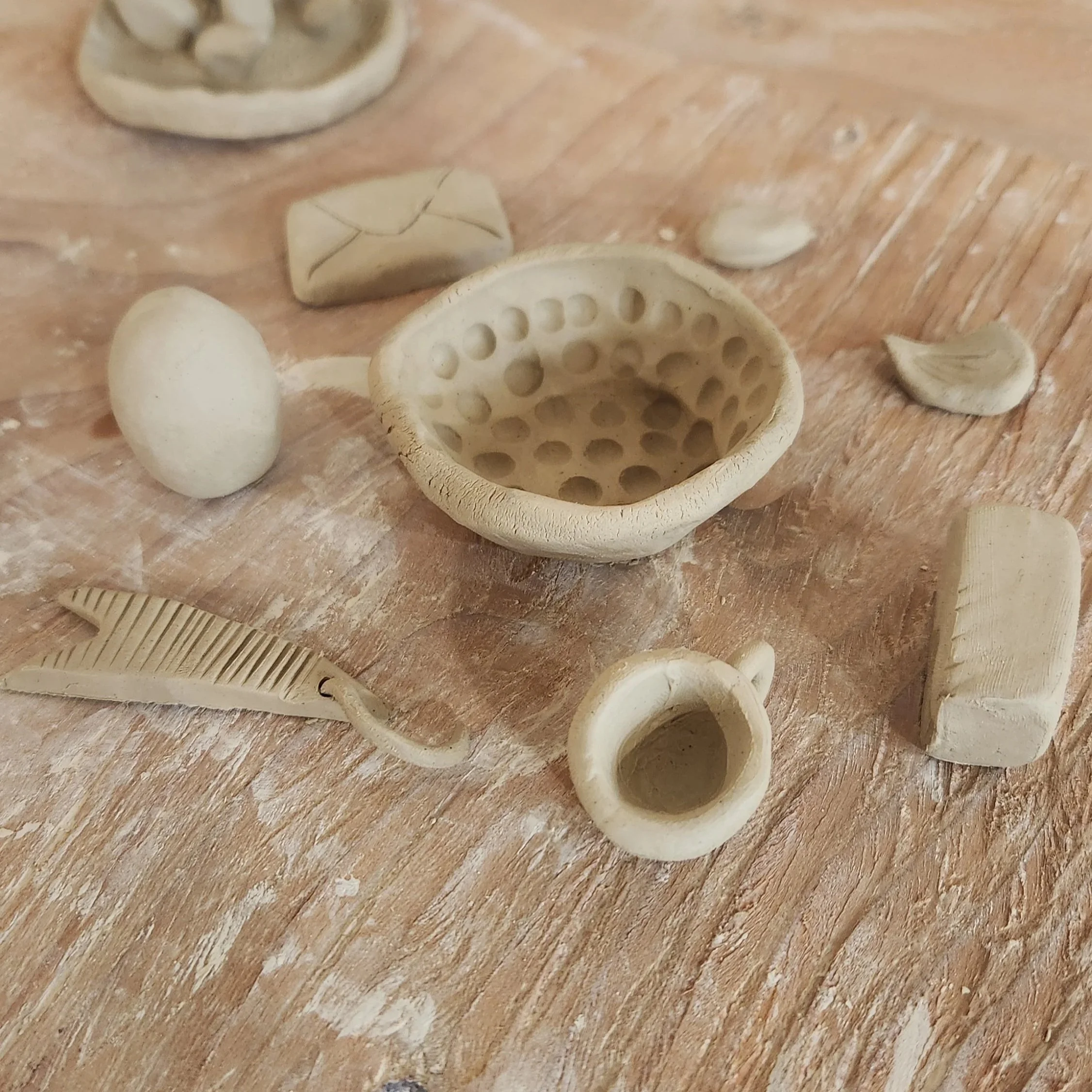 Many handbuilt ceramic pieces sit on a wooden table, waiting to be glazed