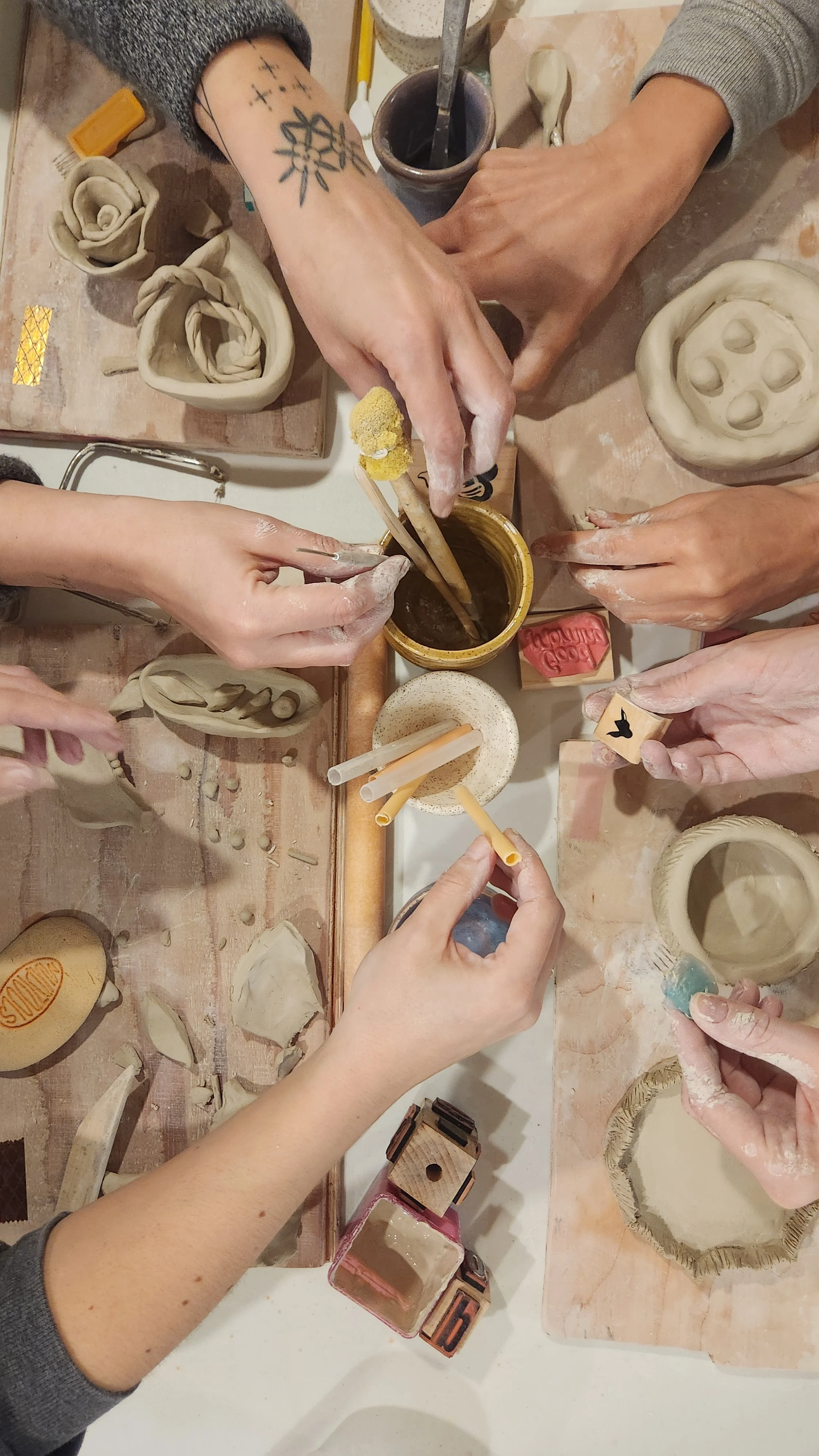 An overhead shot of a group of friends learning about handbuilding pottery techniques at a clay studio in the Bay Area