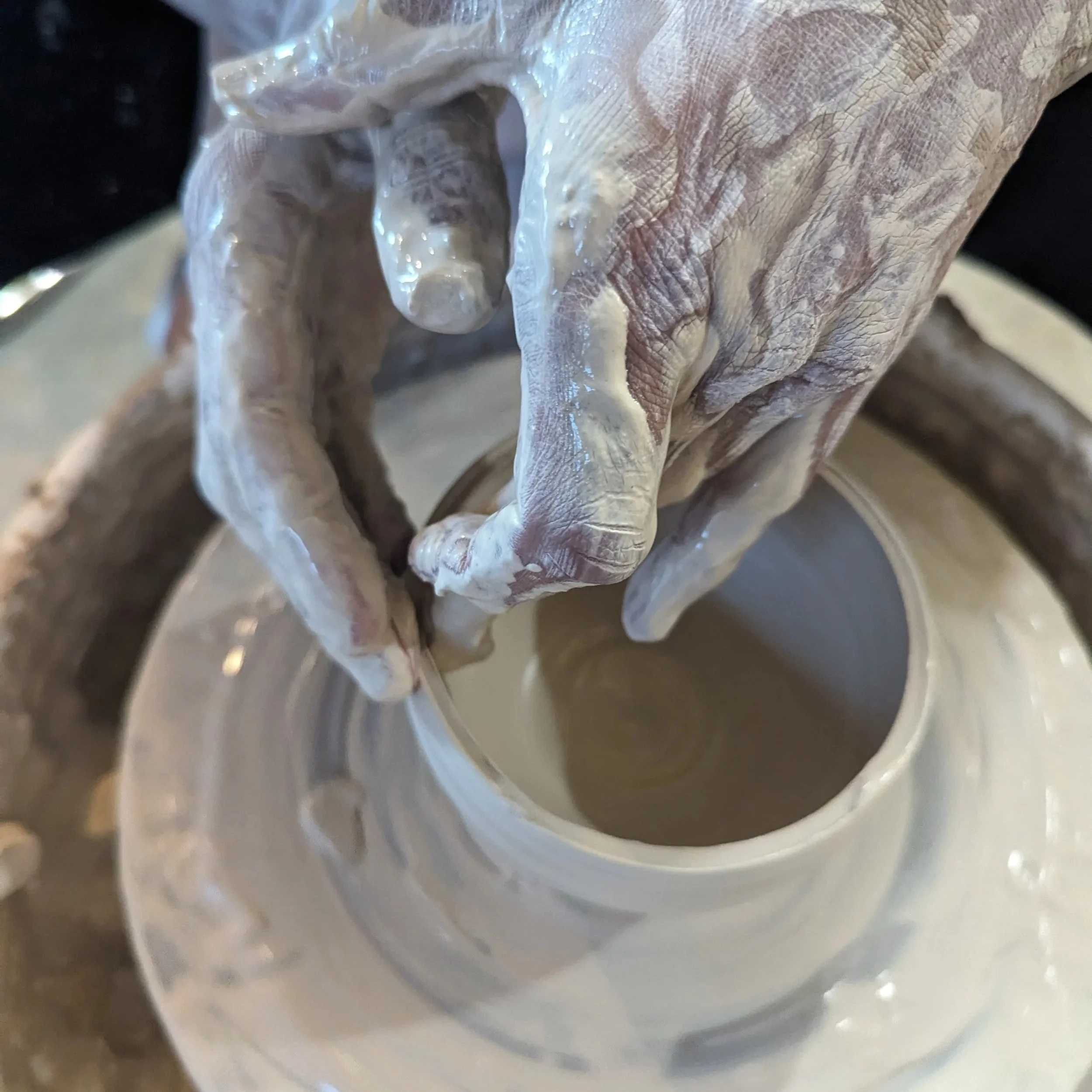 Hands shaping a pot on the potter's wheel in a therapeutic, low stakes beginner chill pottery studio in Oakland