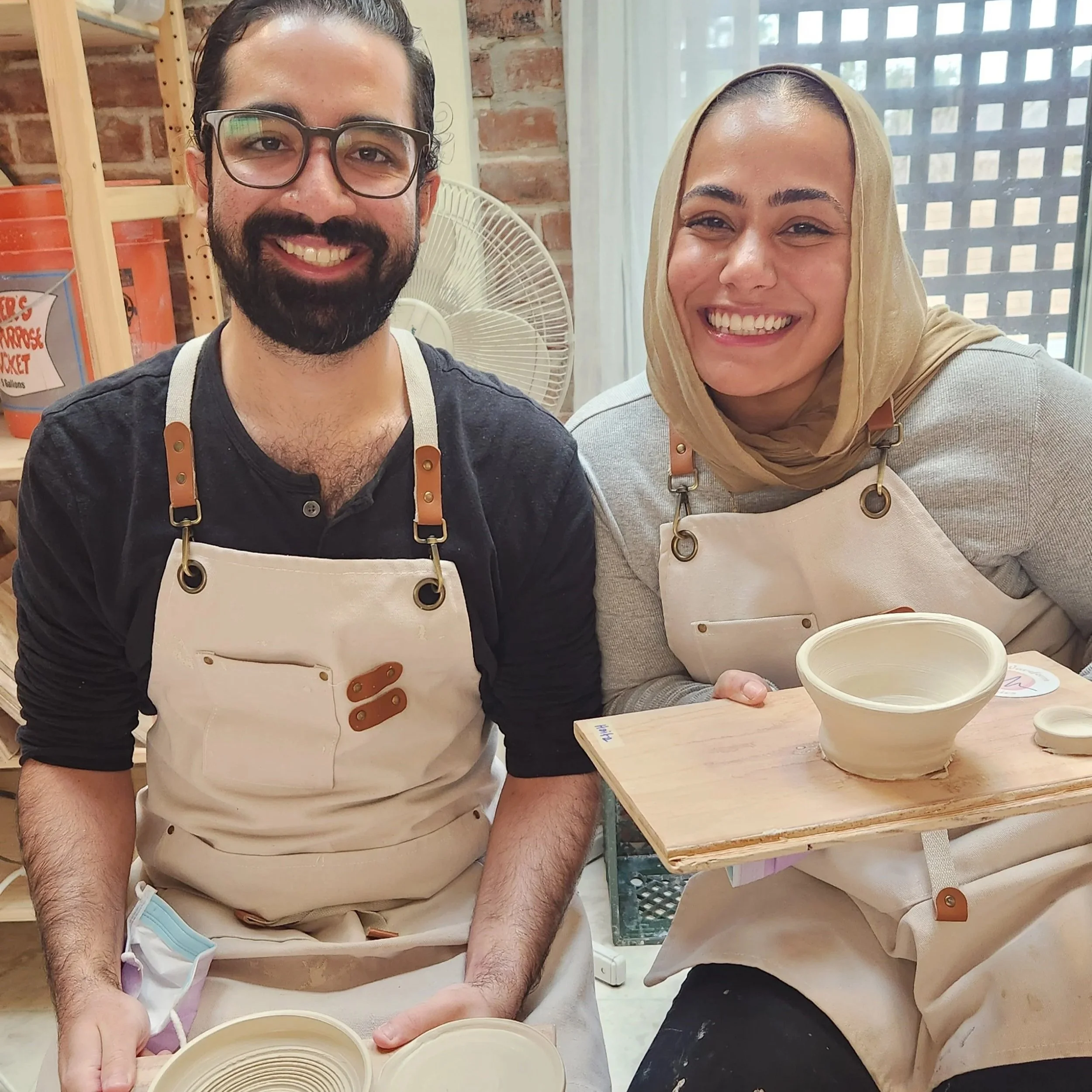 Two beginners having a great time on the potter's wheel making cups and bowls on date night