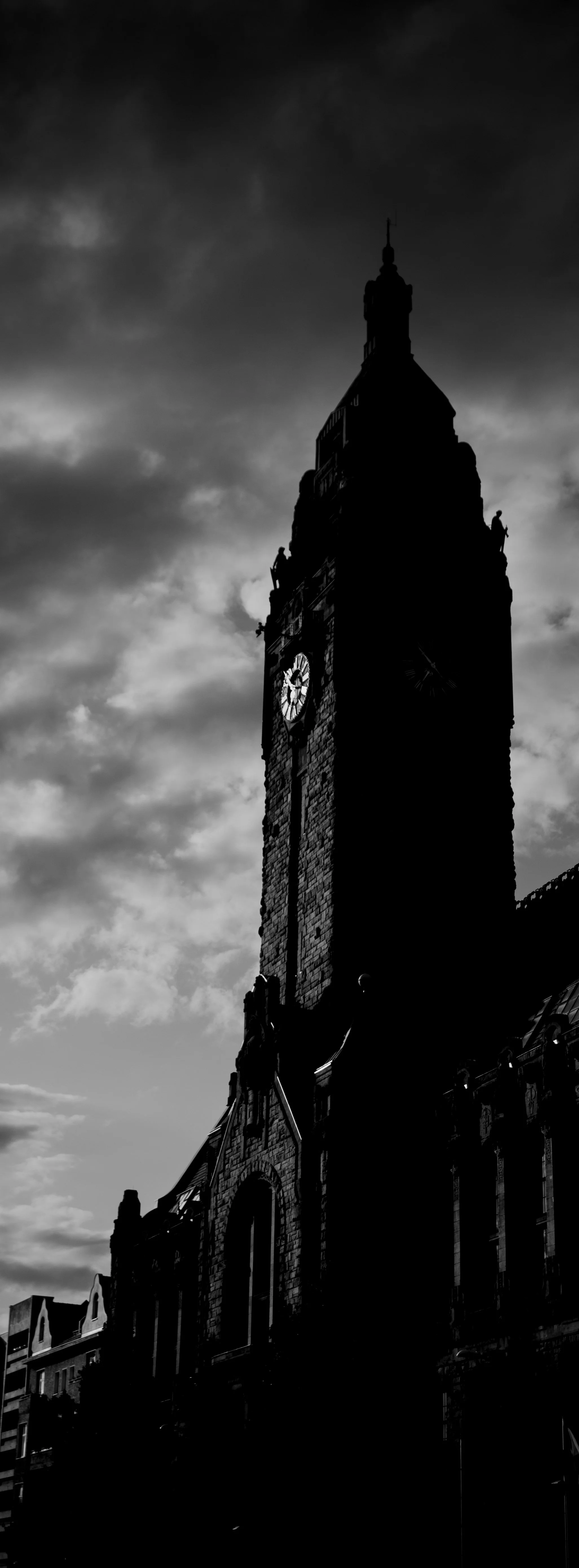 Silhouetted clock tower with cloudy sky in black and white.