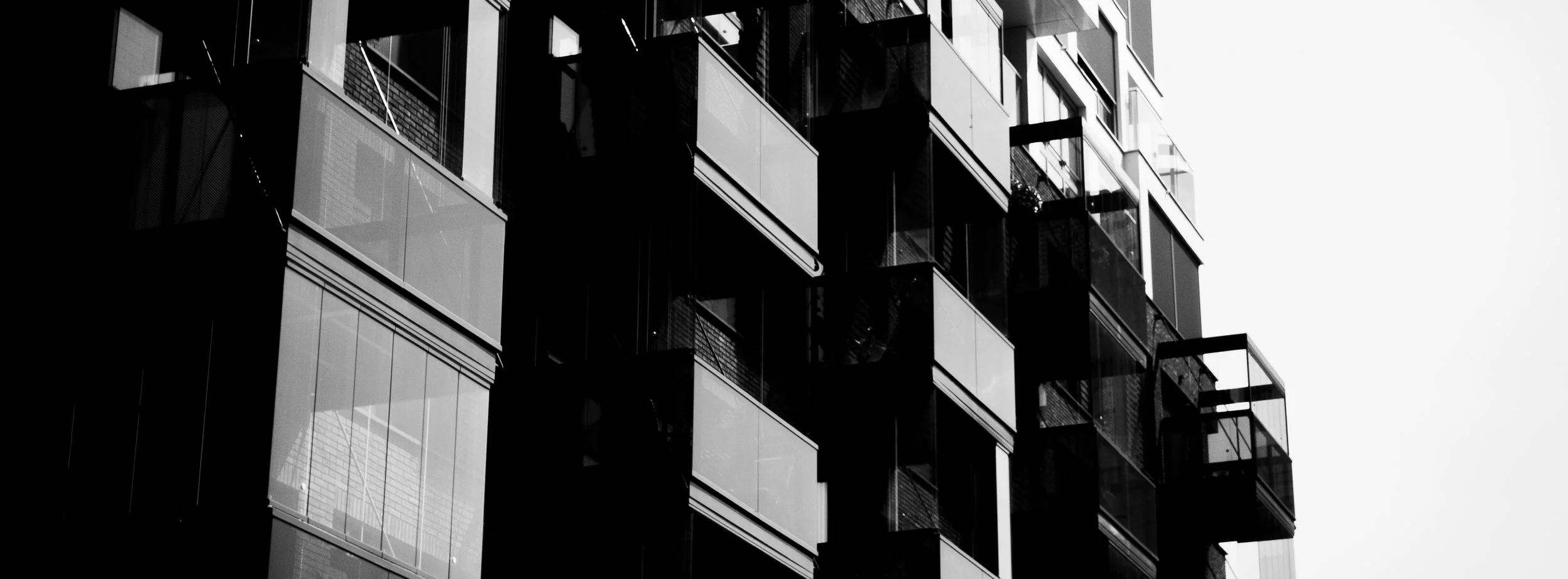 Black and white photo of modern apartment building with glass balconies, showing high-rise structure against a bright sky.