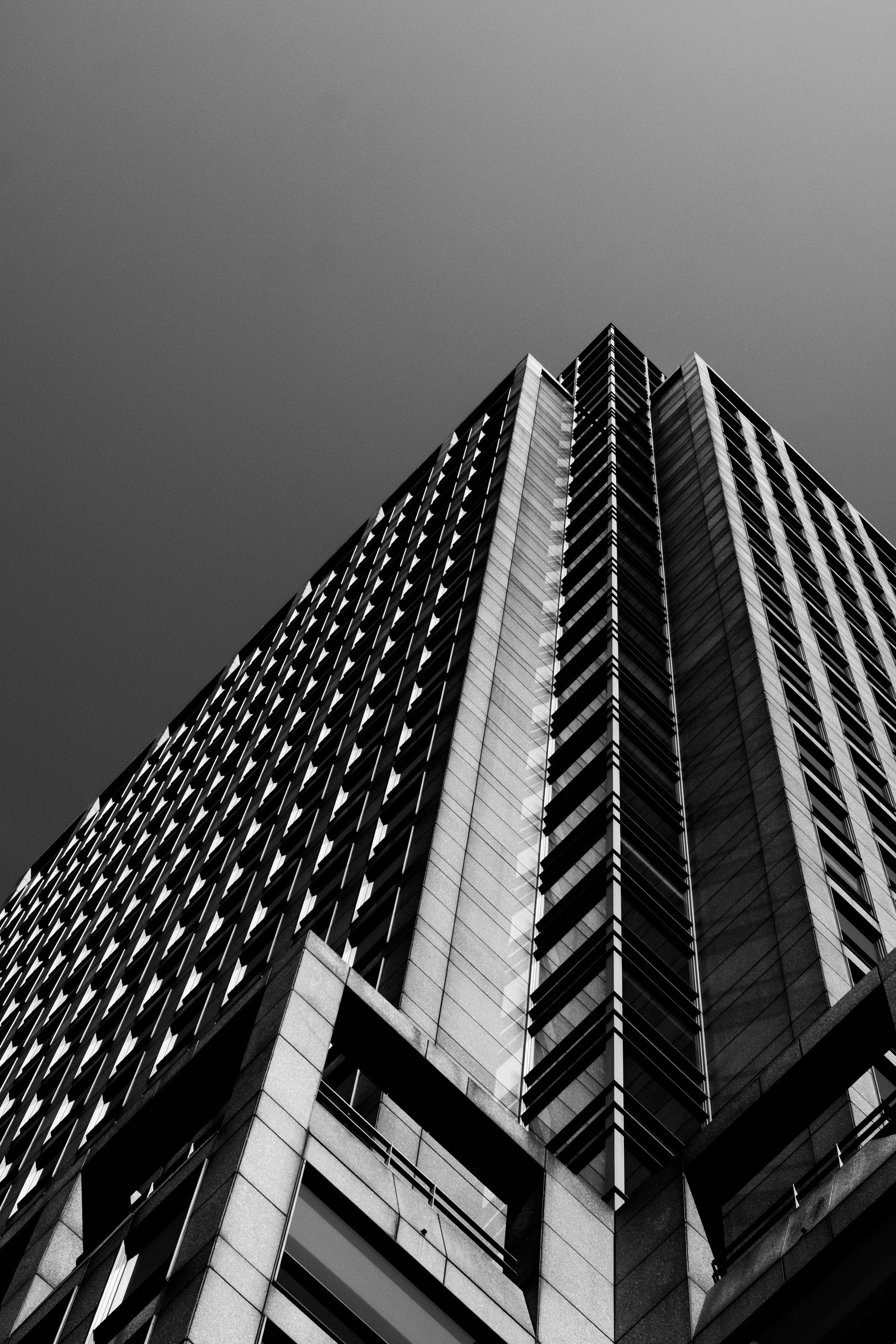 Black and white photo of a modern tall building taken from a low angle, emphasizing its height and geometric architectural design.