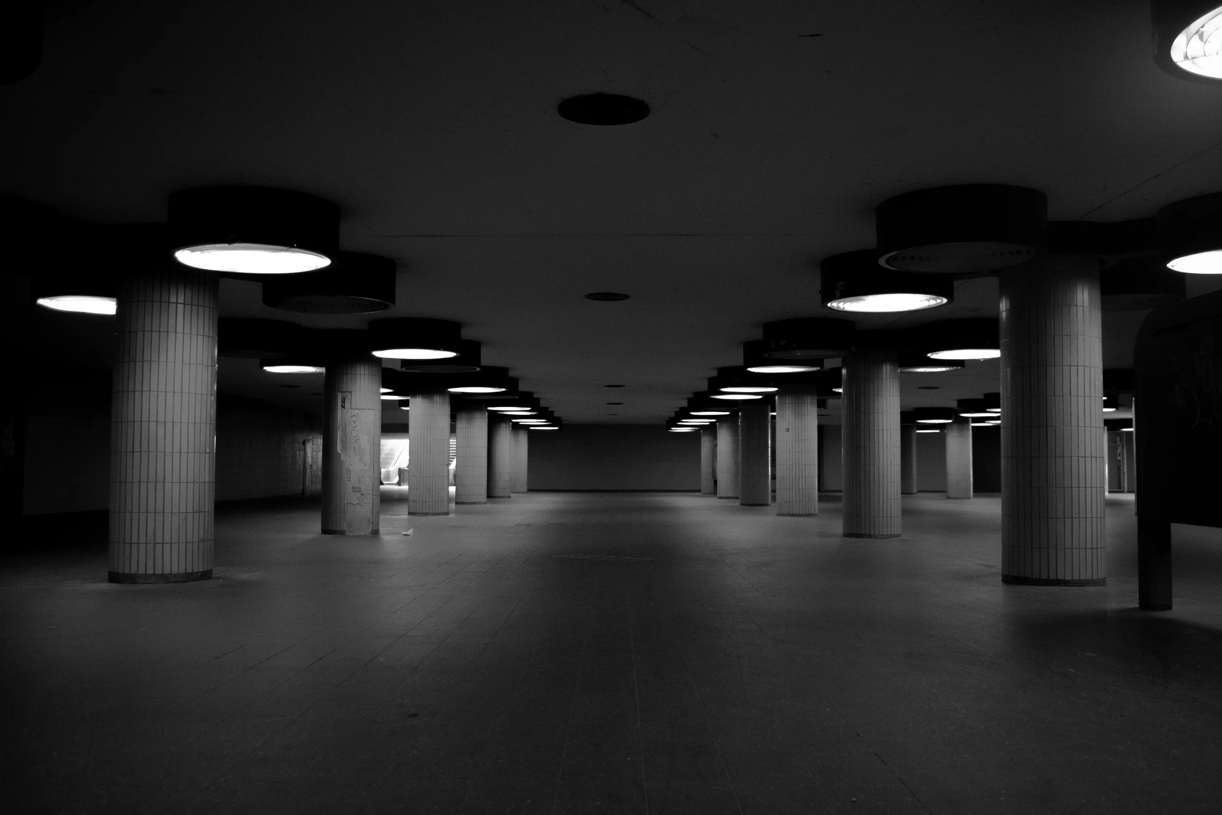 Empty underground subway station with tiles on columns and circular ceiling lights.