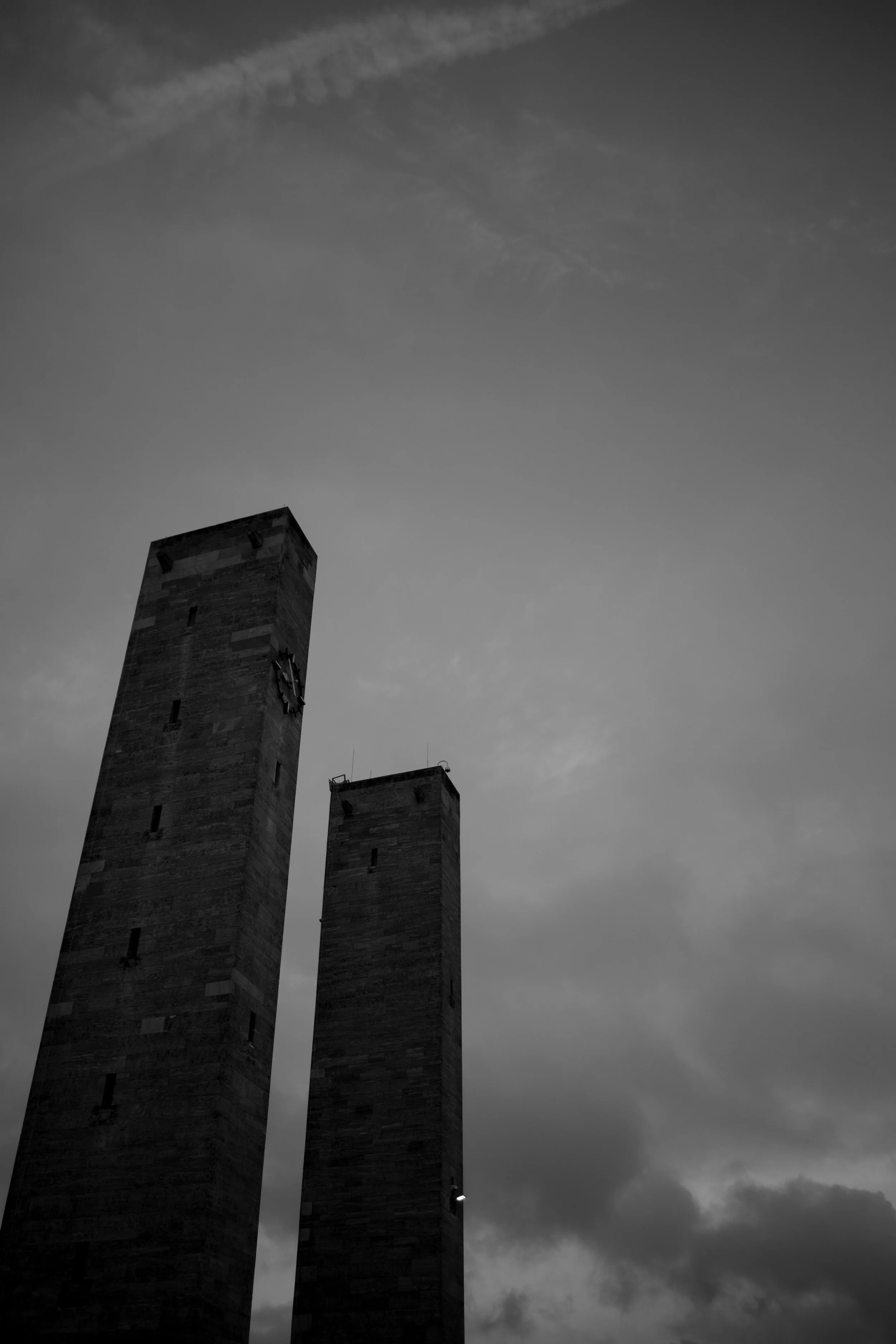 Two tall stone towers under a cloudy sky, one with a clock on it.