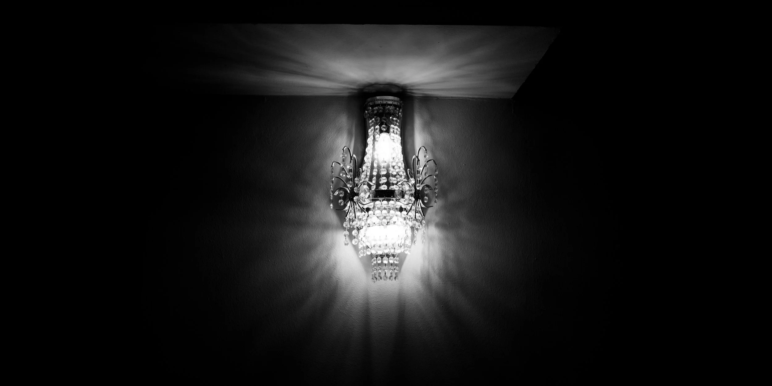 A decorative chandelier mounted on a wall, emitting light that creates a pattern of shadows on the ceiling.