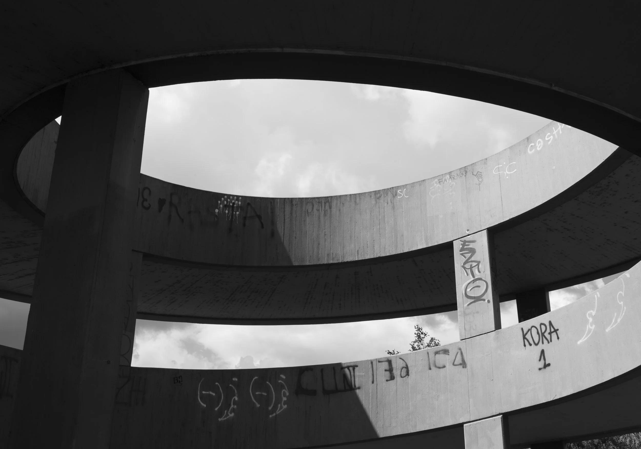 Concrete spiral structure with graffiti, opening to a cloudy sky.