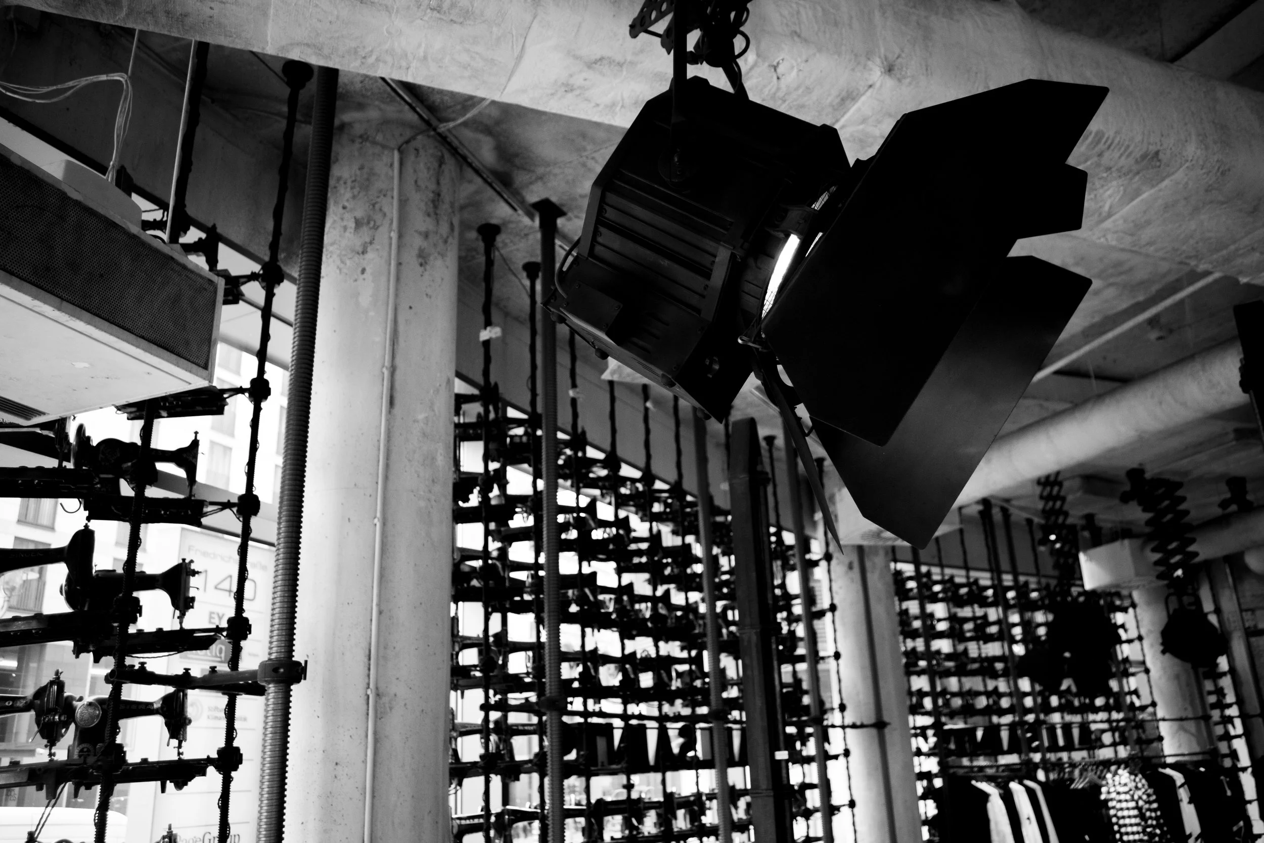 Black and white image of studio lighting fixtures hanging from the ceiling of an industrial-style space with large windows and walls.