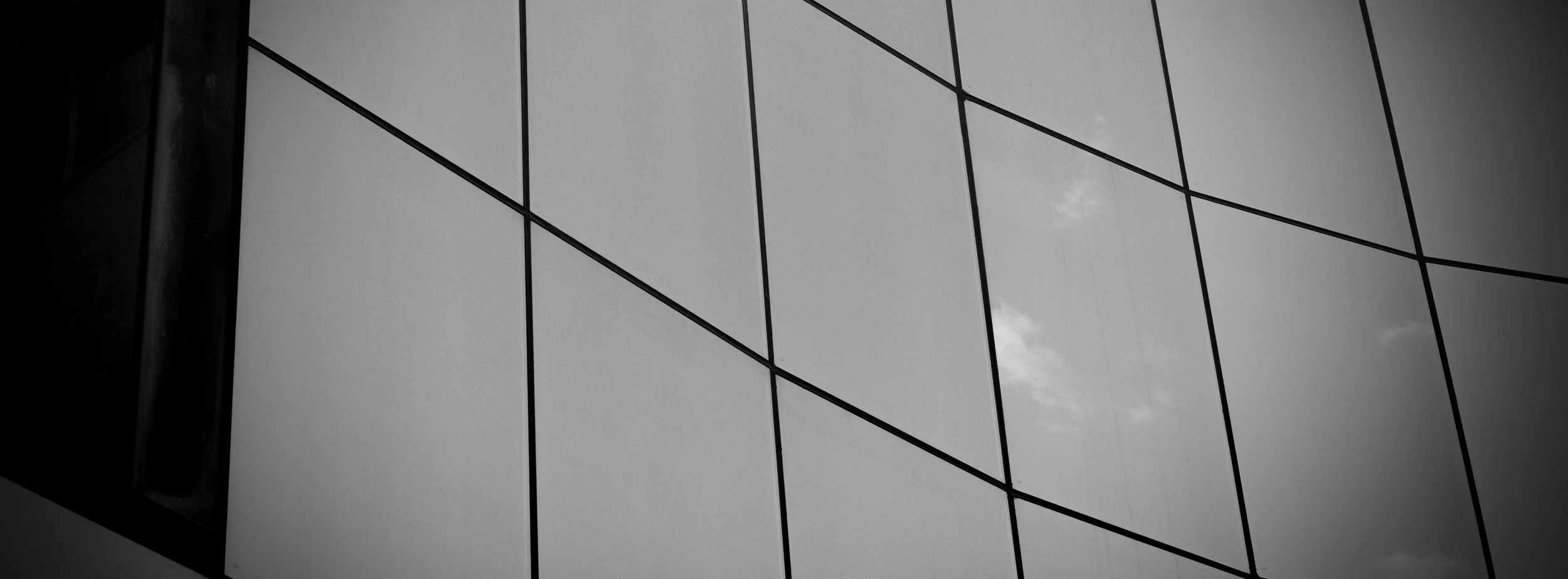 Close-up view of a modern glass building facade with reflective windows, showing a cloudy sky reflected in the glass.