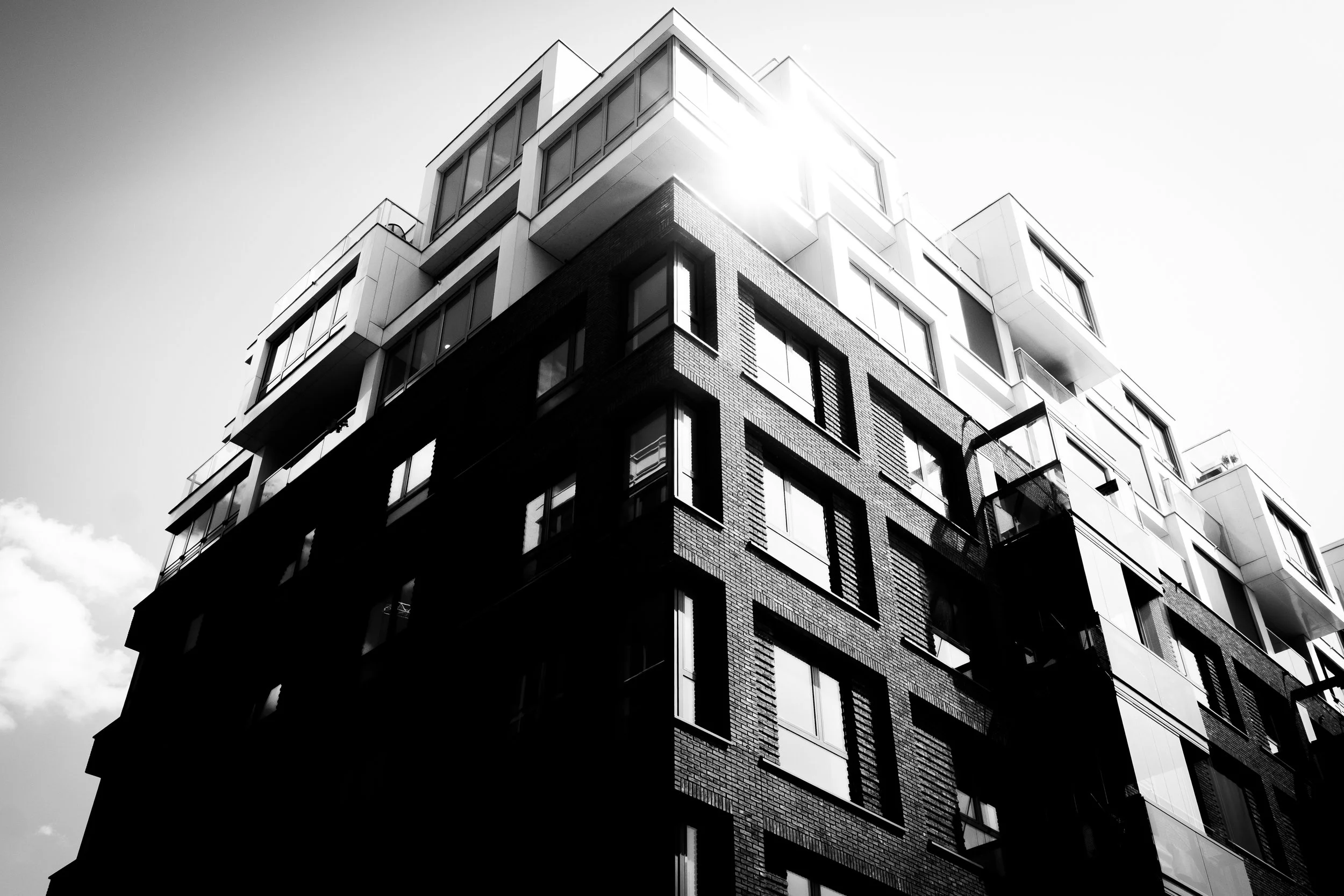 Black and white photo of modern multi-story apartment building with prominent windows and balconies, sun shining from behind the top corner.