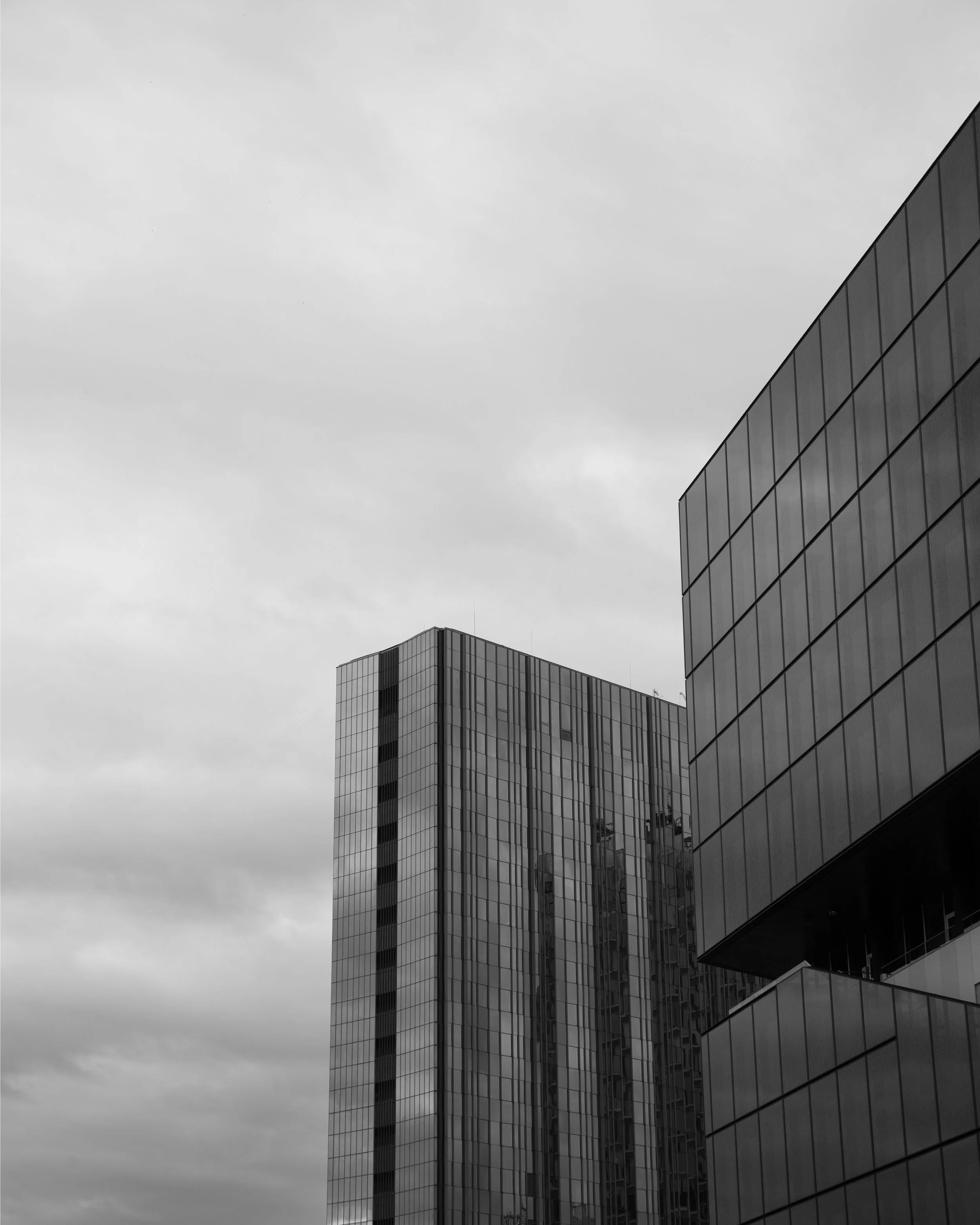 Black and white photo of modern glass skyscrapers against cloudy sky.