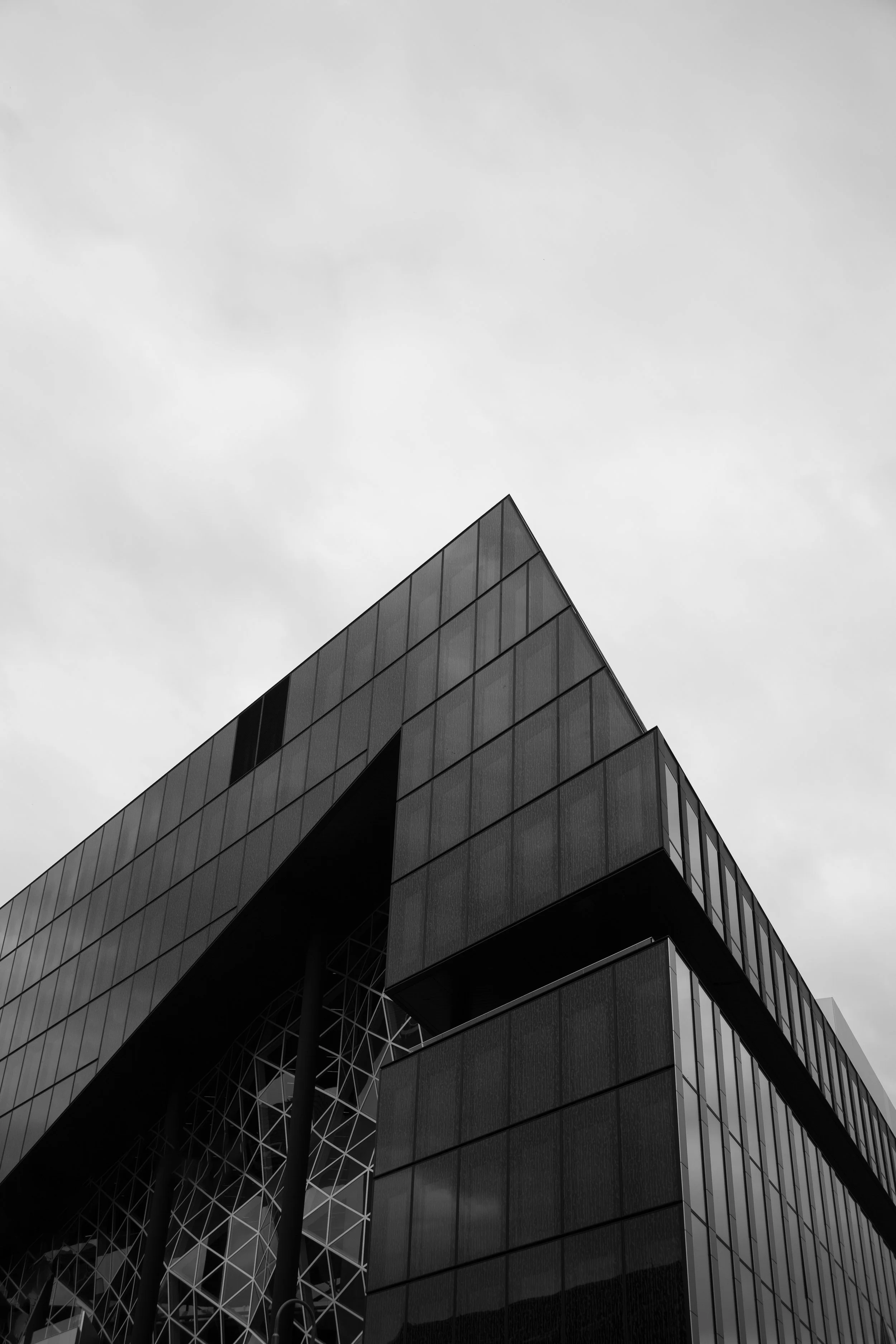 Black and white photo of a modern, angular building with glass windows and metal panels, under a cloudy sky.