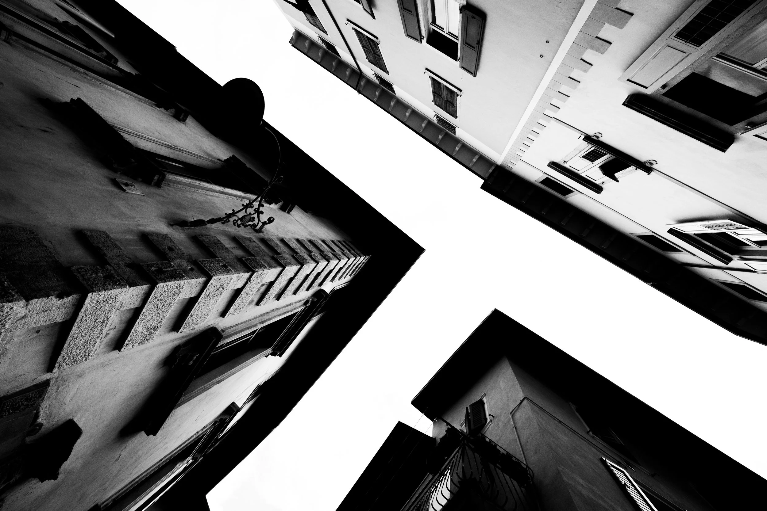 Black and white photo taken from ground level looking up at tall buildings with open sky visible between them.