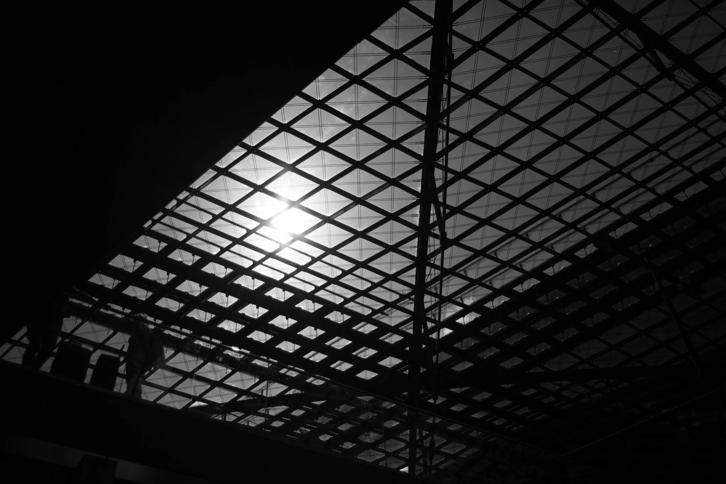 Interior of a modern building with a glass ceiling and metal framework, with sunlight partially visible through the ceiling.