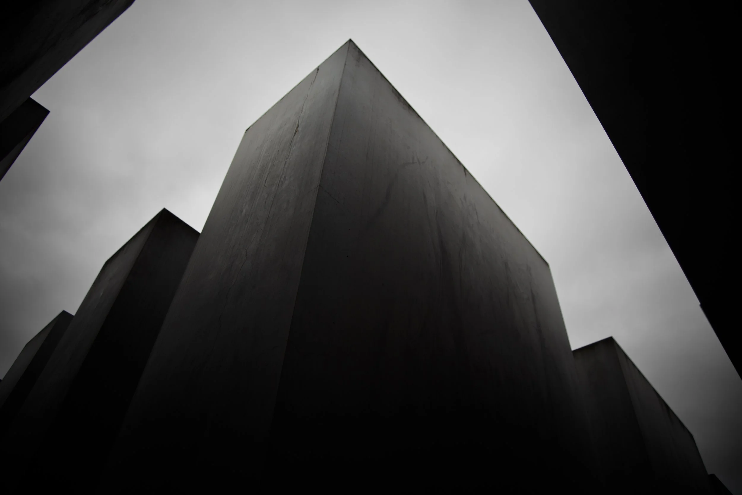 Low-angle view of tall, dark concrete buildings with a cloudy gray sky overhead.