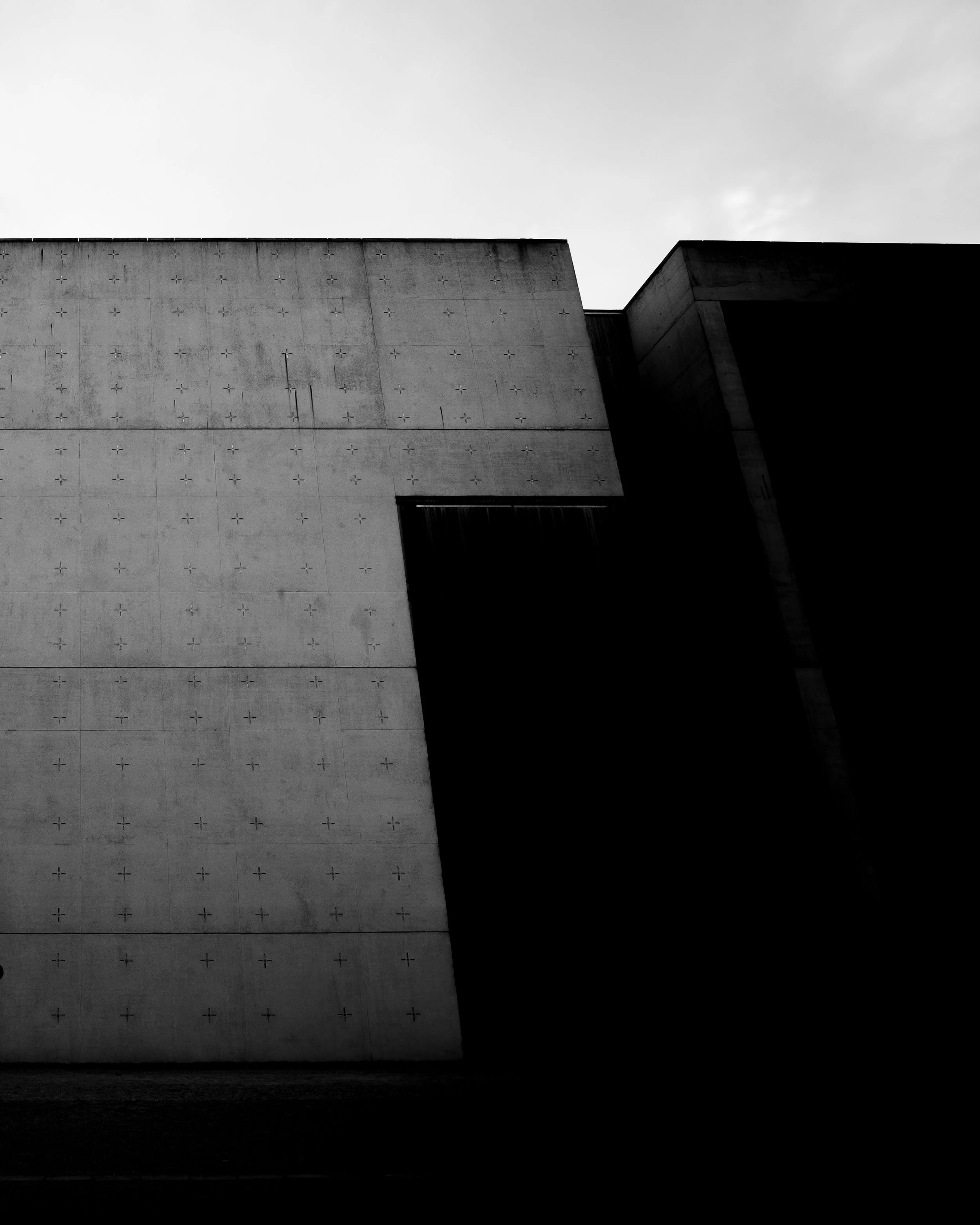 Black and white photo of a modern concrete building with geometric shapes and minimal design, under a cloudy sky.
