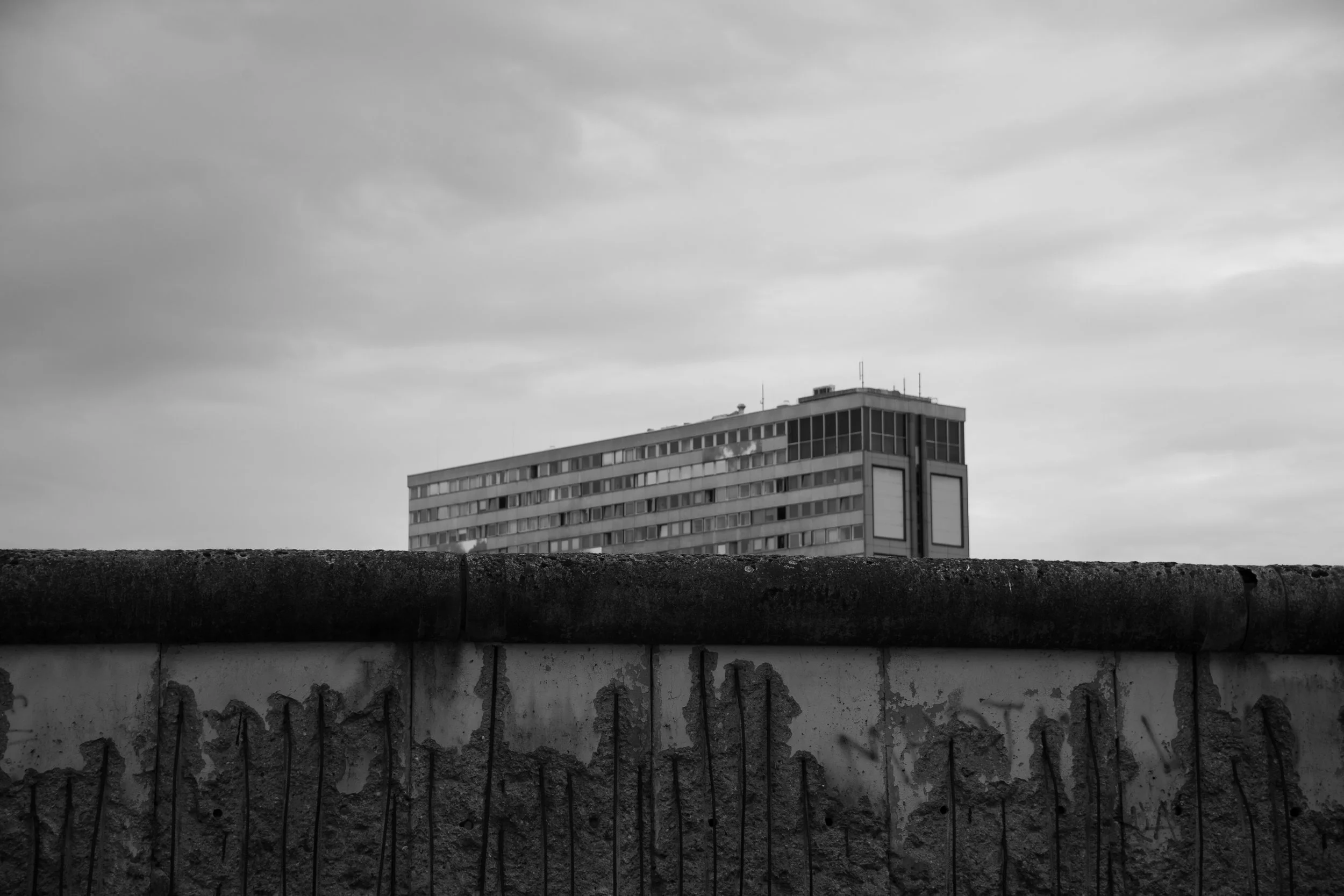 Black and white photo of a high-rise building behind a concrete wall with graffiti. The sky is cloudy.