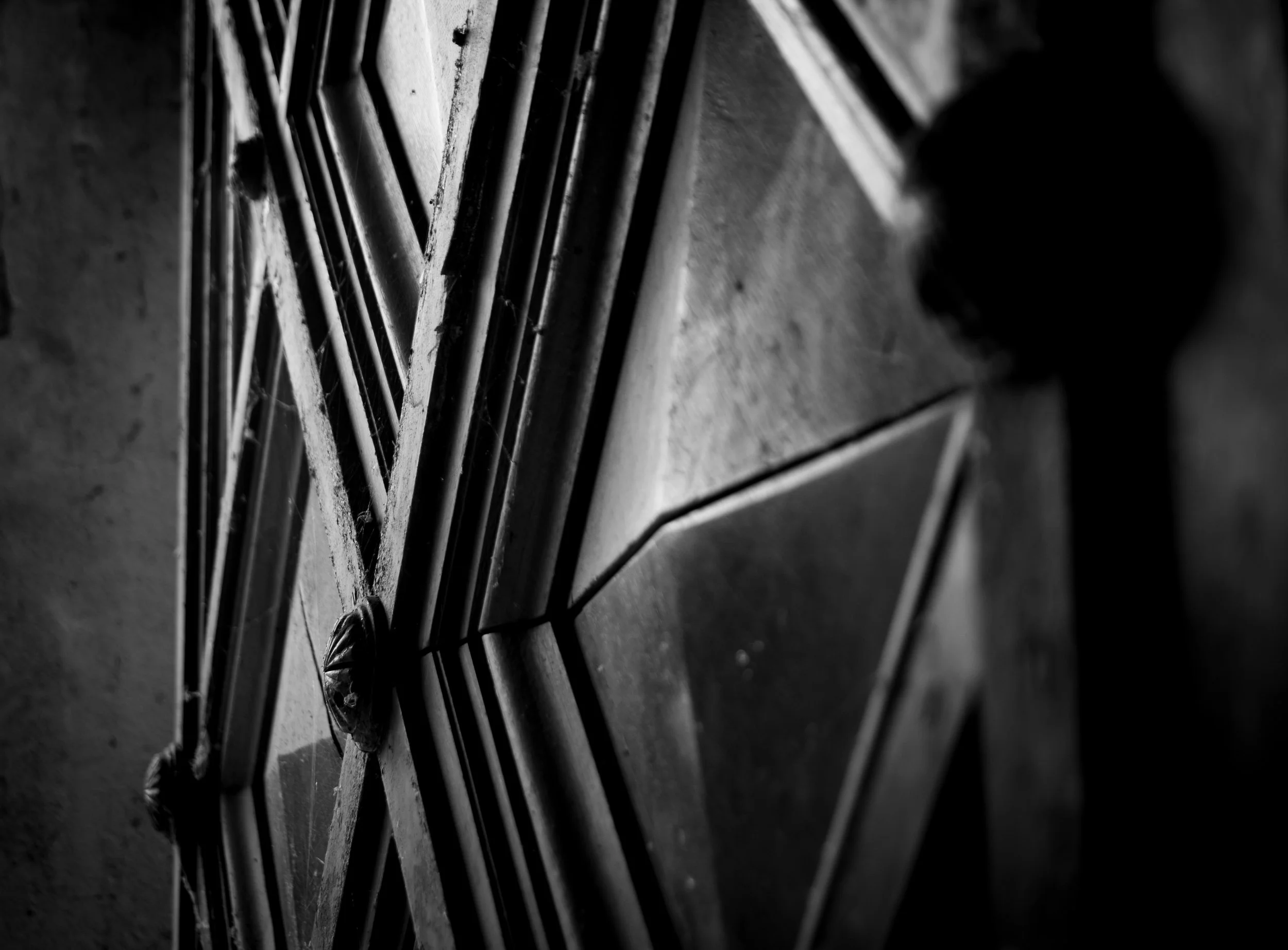 Black and white close-up of a metal door with a star-shaped design, attached to a textured wall.