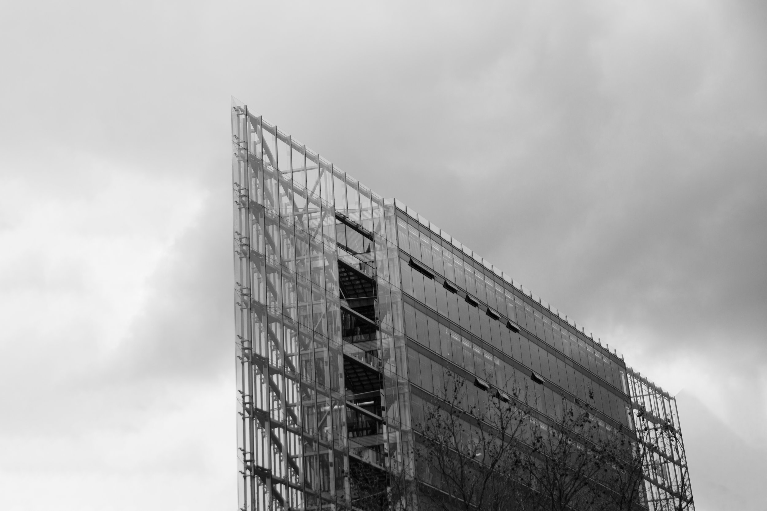 A modern multi-story building with a glass facade and open staircase, set against a cloudy sky.