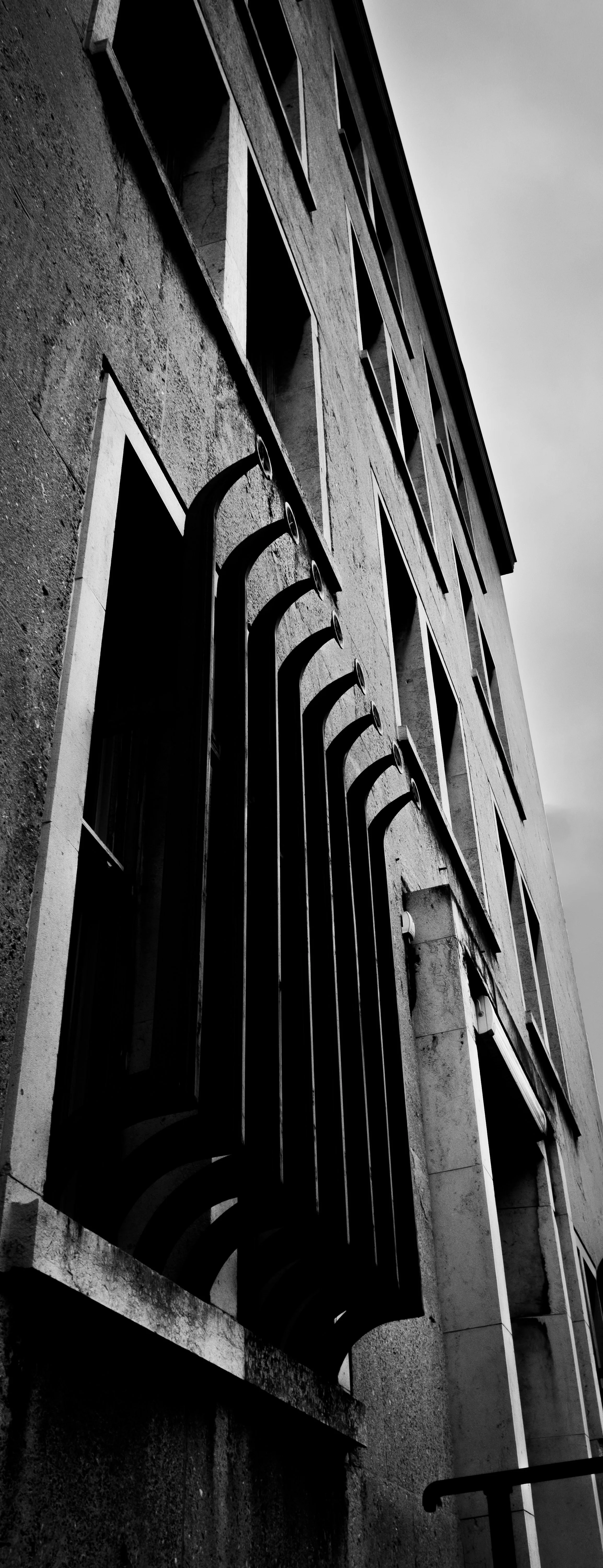 Black and white photo of a multi-story building's exterior with multiple windows and decorative metal bars, taken from a low angle.