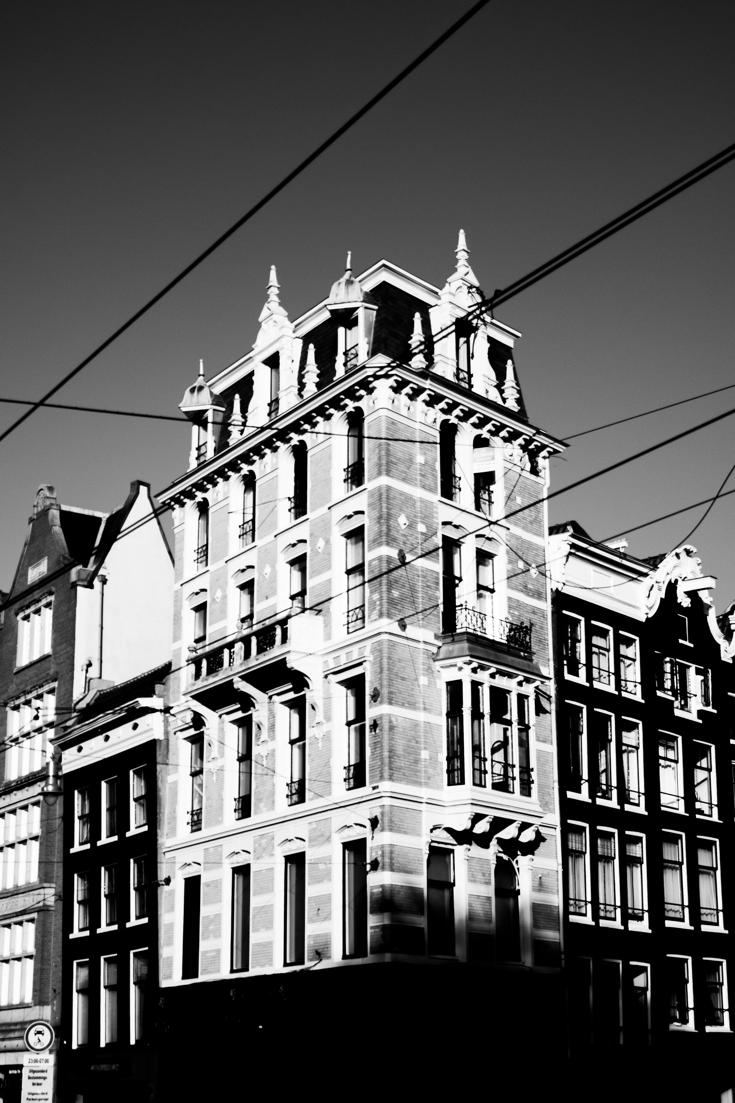 Black and white photo of an ornate multi-story building with decorative architectural details, including turrets and large windows, with overhead wires crossing the sky.