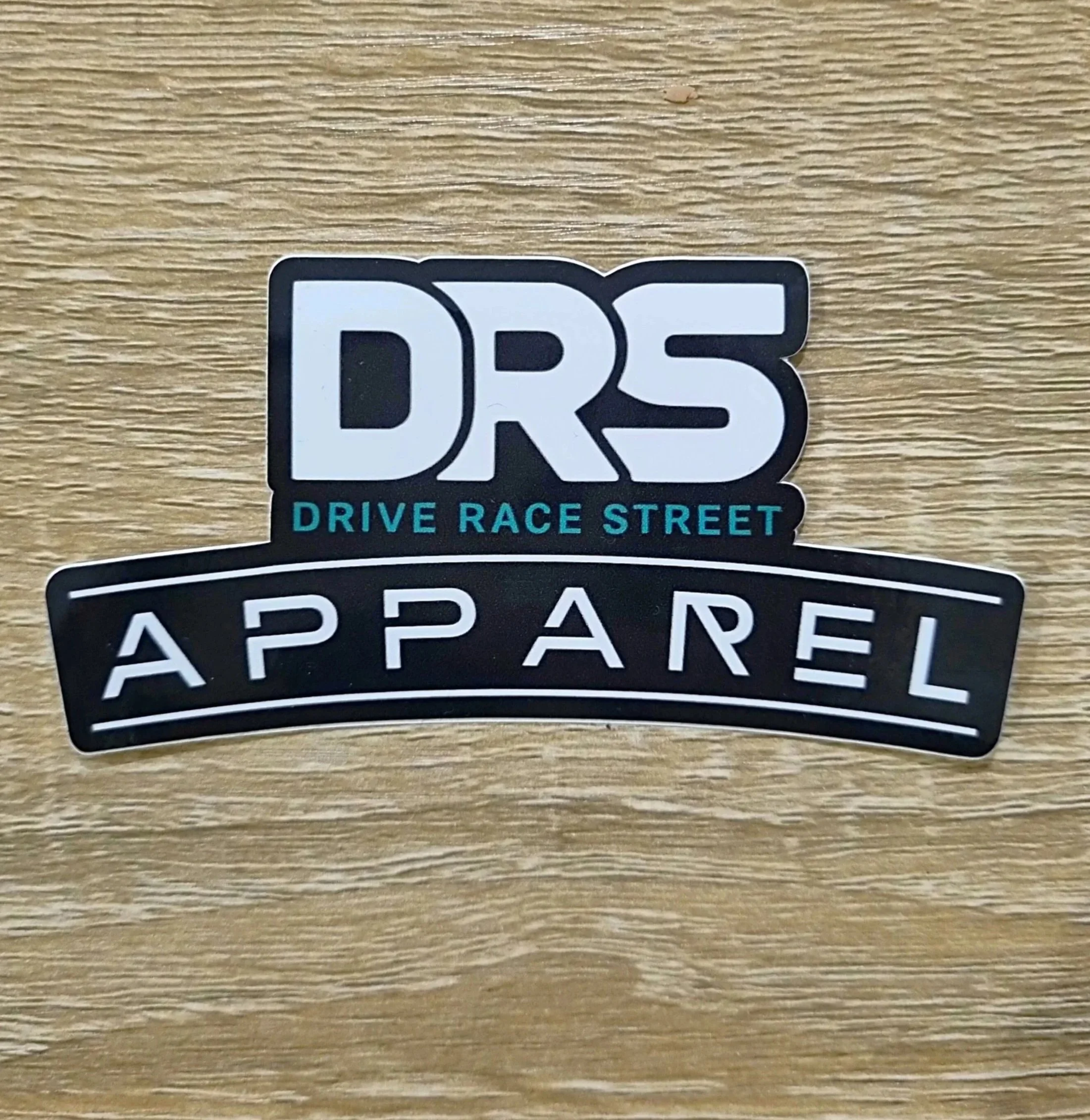 DRS Apparel official logo sticker in high-quality waterproof vinyl, featuring white and teal typography on a durable black background for automotive use, laptops, bottles, books.