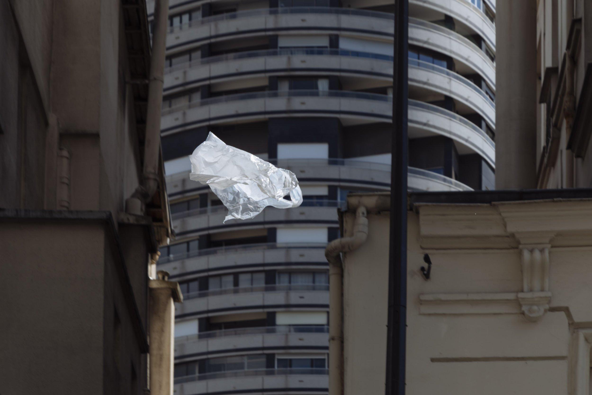 A crumpled piece of aluminum foil floating between tall buildings in an urban setting.