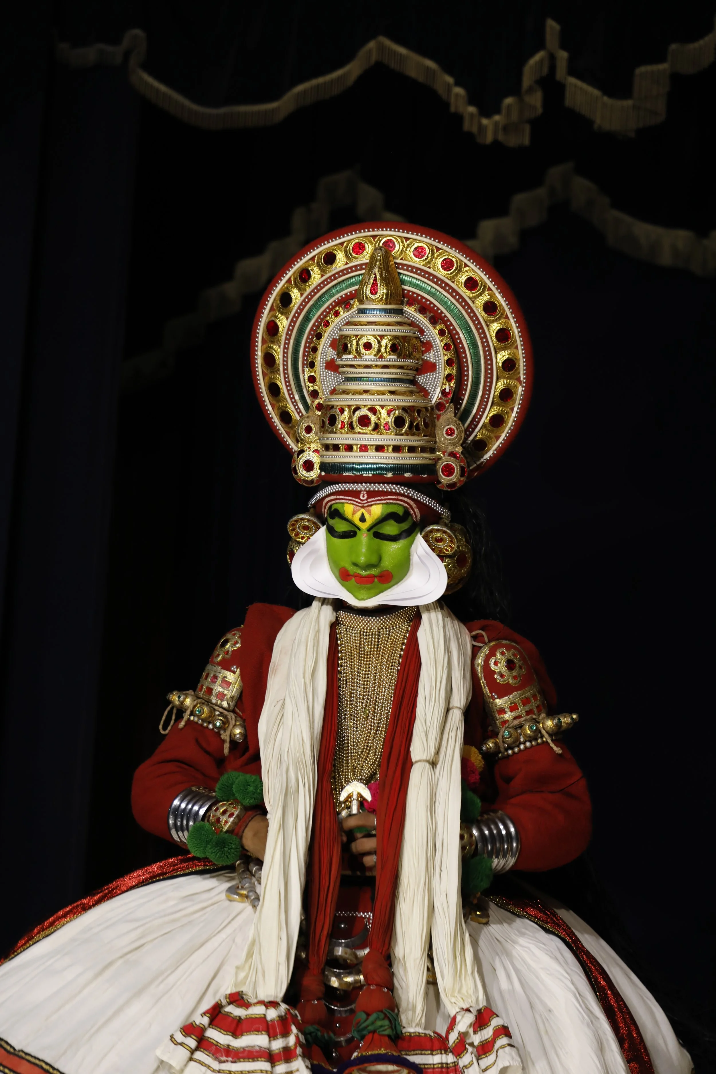 A traditional performance puppet with a green face, dressed in ornate clothing and a large decorative headpiece.
