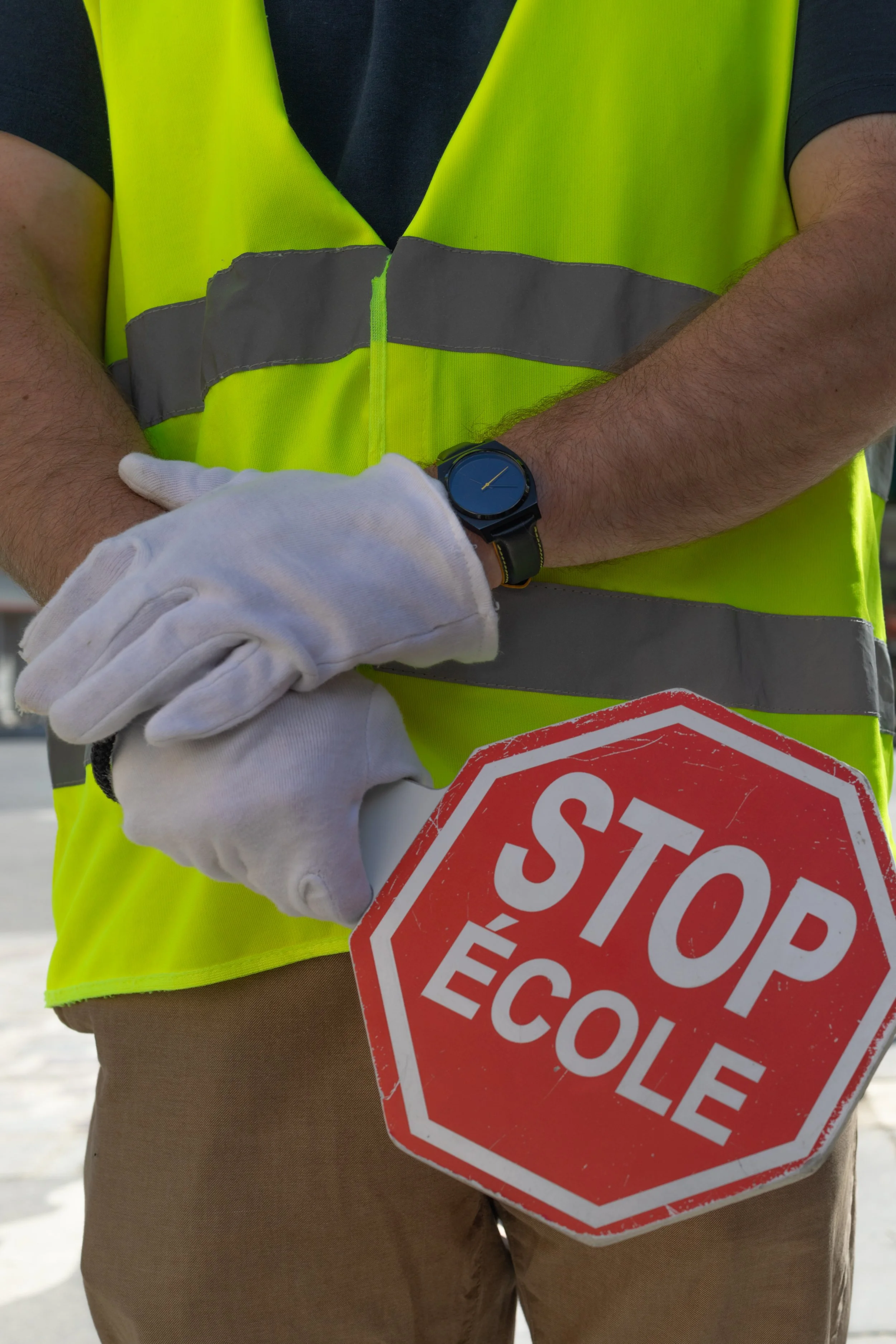 Person wearing a yellow safety vest holding a stop sign with French text, 'STOP ÉCOLÉ', outdoors.