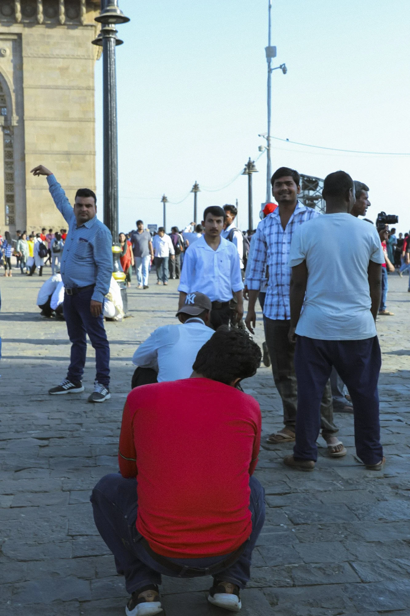 People gathered outdoors near a historical monument with a large crowd in the background.