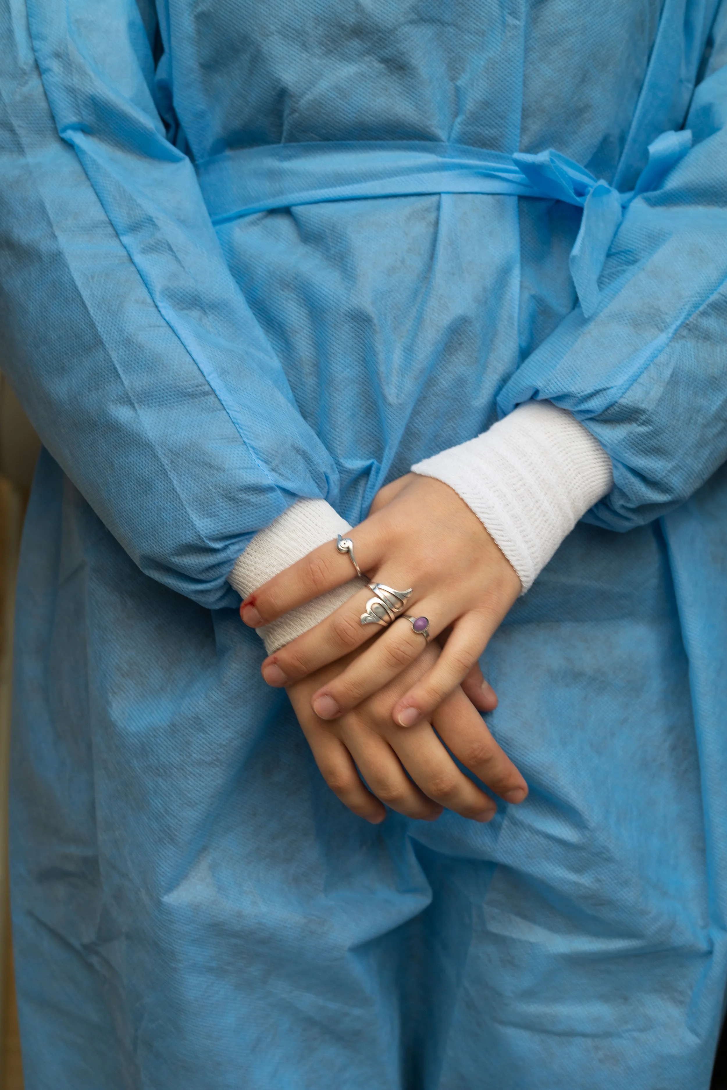Hands of a person wearing multiple rings, with arms crossed over a blue medical gown.