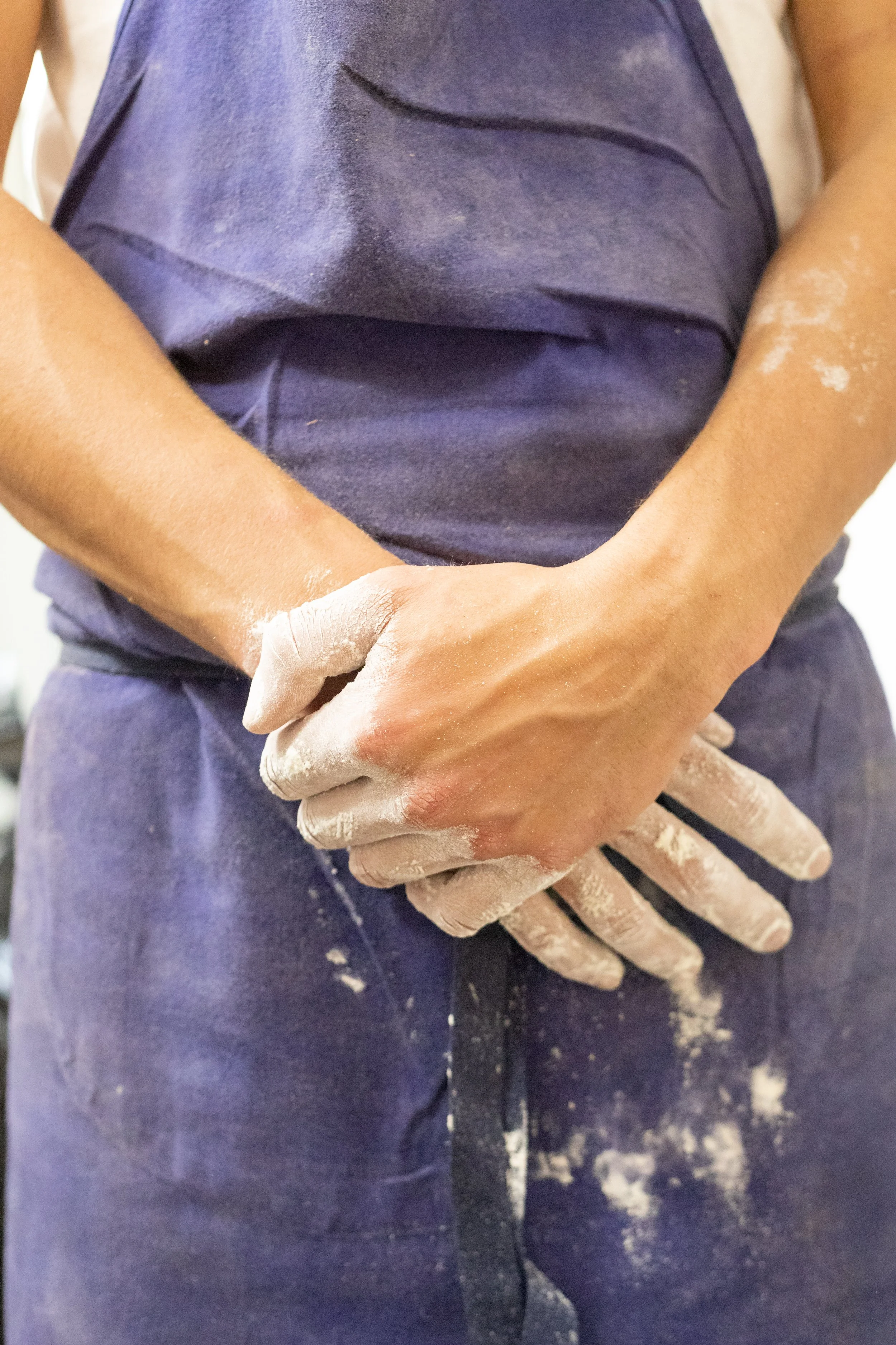 A person wearing a blue shirt and matching pants with flour on their skin and clothing, and hands clasped together with white flour.