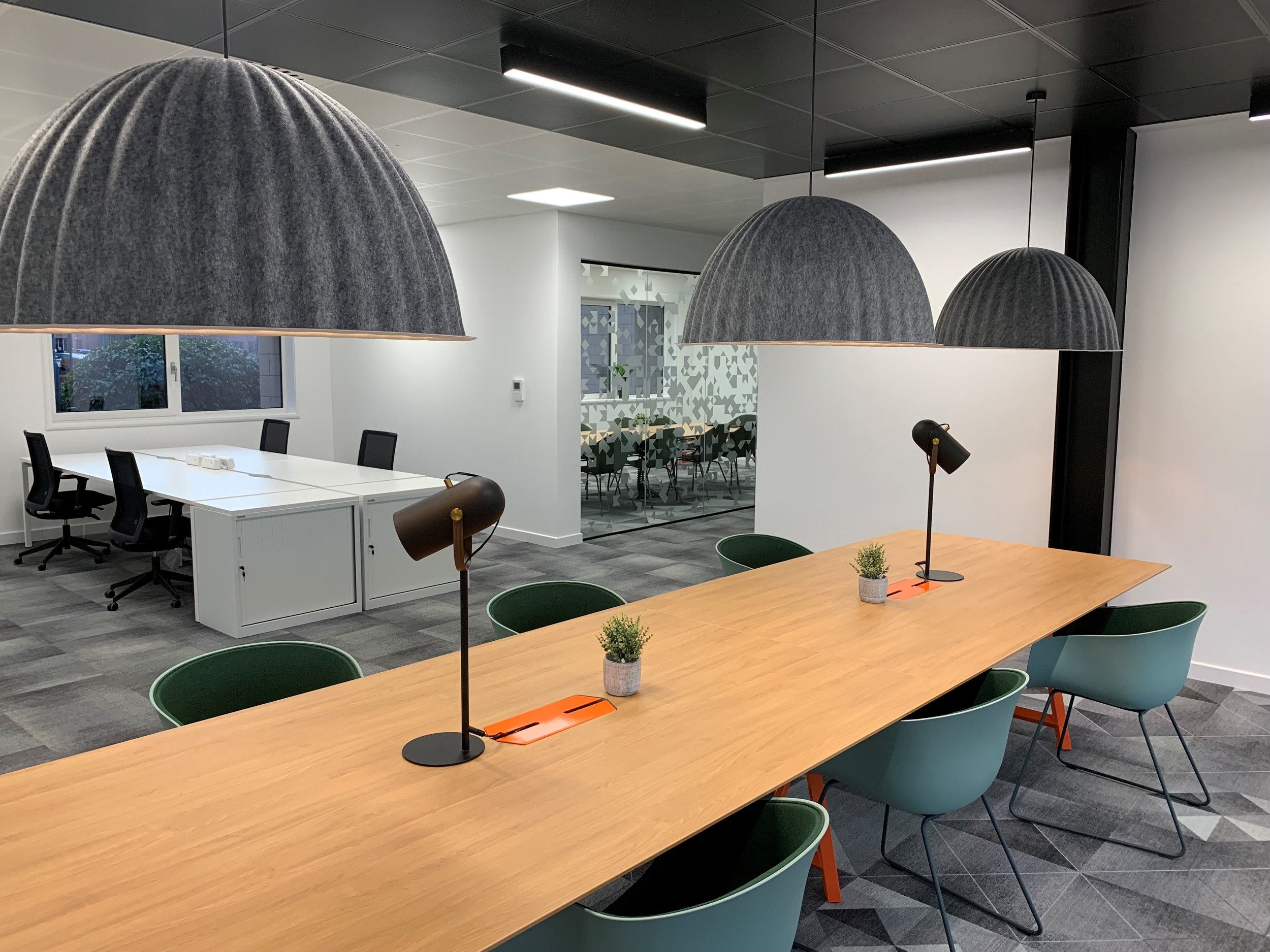 Modern office space with a long wooden table, green chairs, and hanging pendant lights, part of an office fit-out by GM Projects.